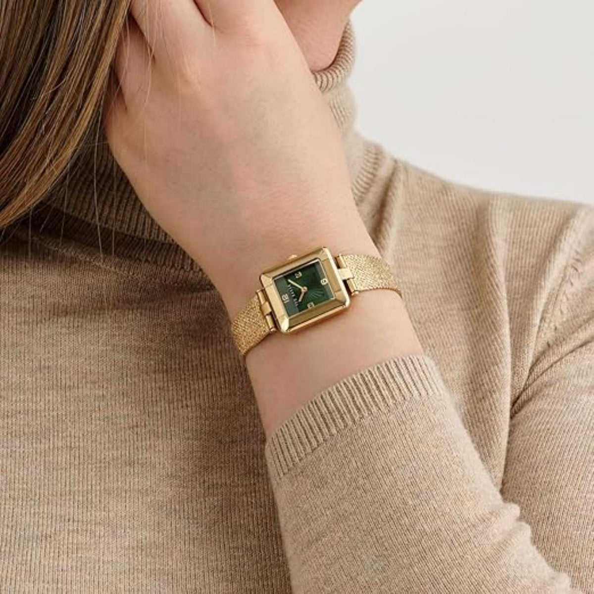 Model wearing gold mesh strap watch with green dial and gold case
