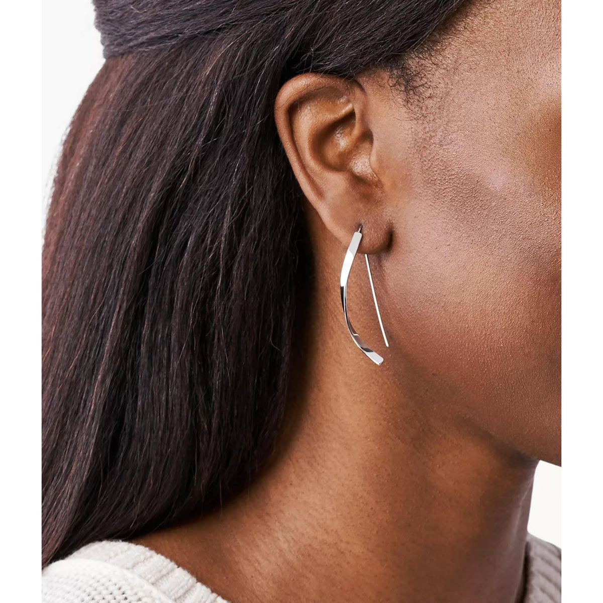 Worn silver-tone hoop earrings, curved open-link dangle hanging from earlobe