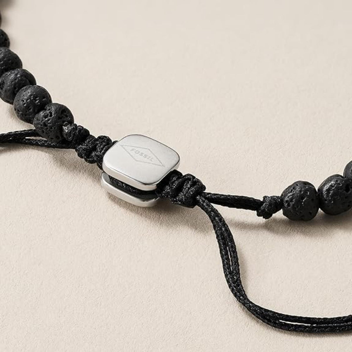 Close-up of men's black bead bracelet with silver-tone square logo tag and cord tie