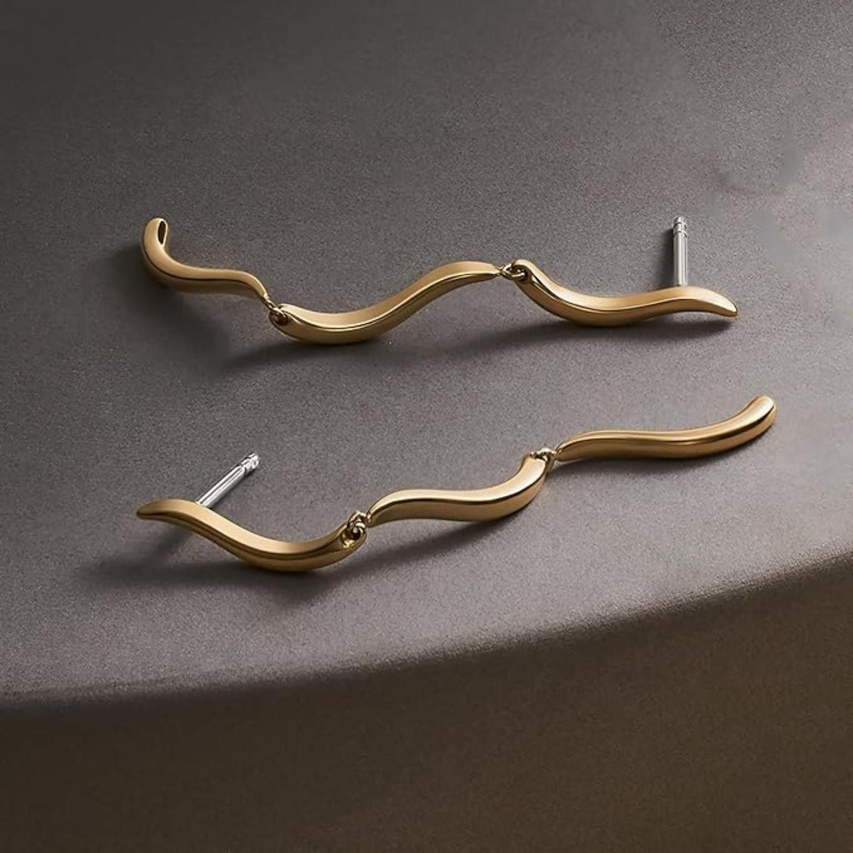 Gold-tone wave drop earrings shown laid out, stud posts with wavy curved bars