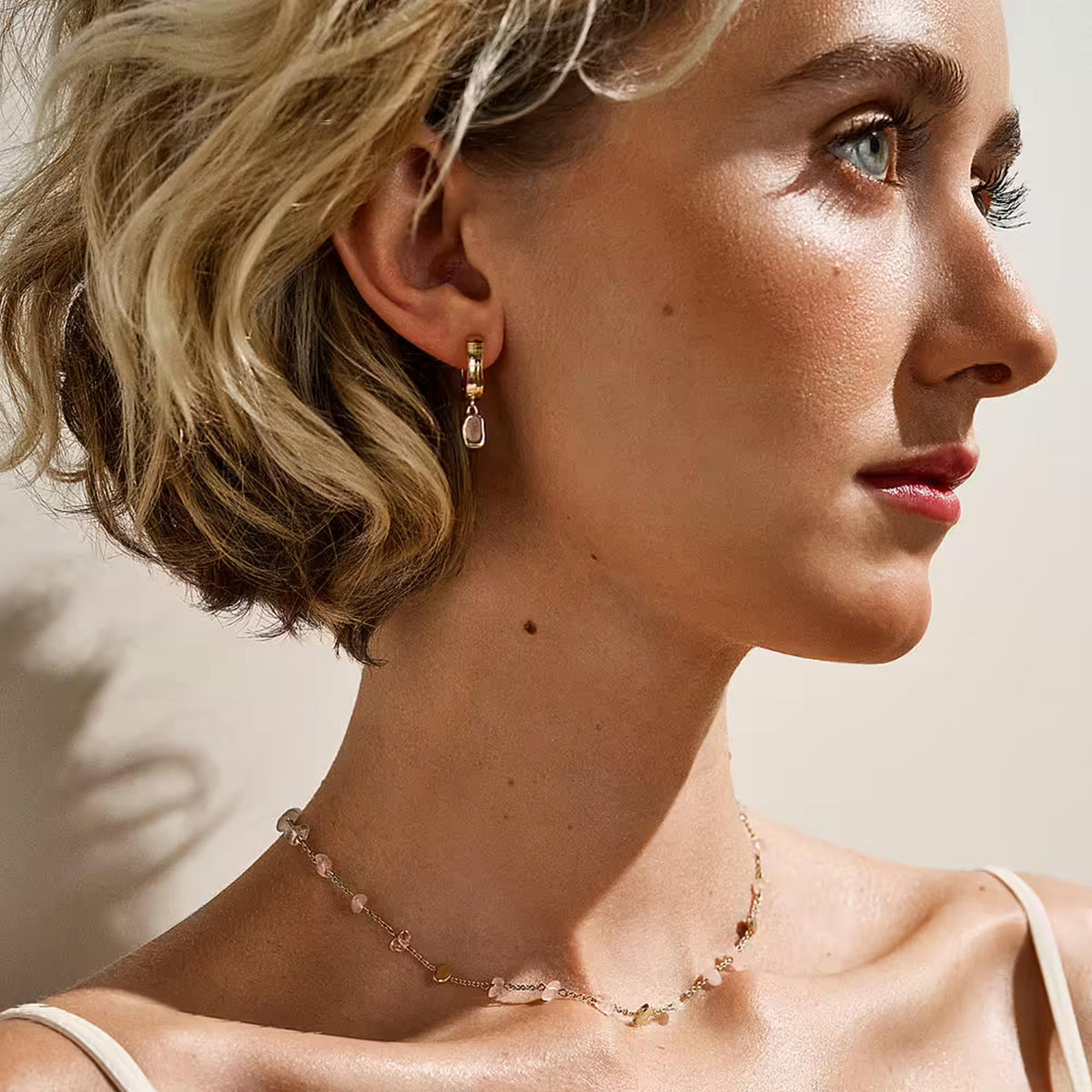 Gold-tone rose quartz hoop earrings worn by model with pink gemstone dangles