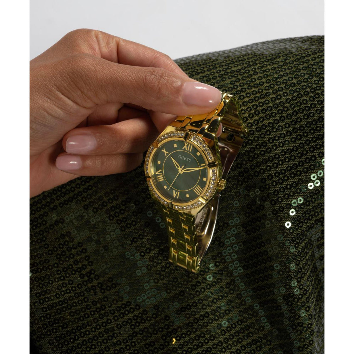Gold-tone watch held near wrist, green dial with crystal bezel and gold hands