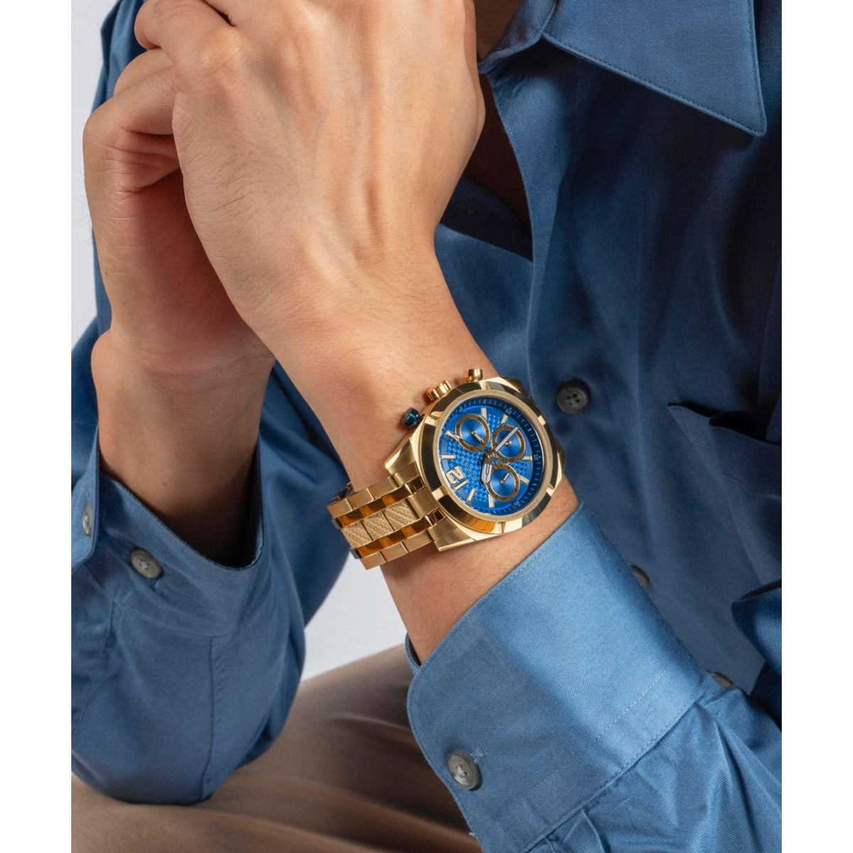 Men's gold-tone stainless steel watch with blue dial and metal bracelet on wrist.