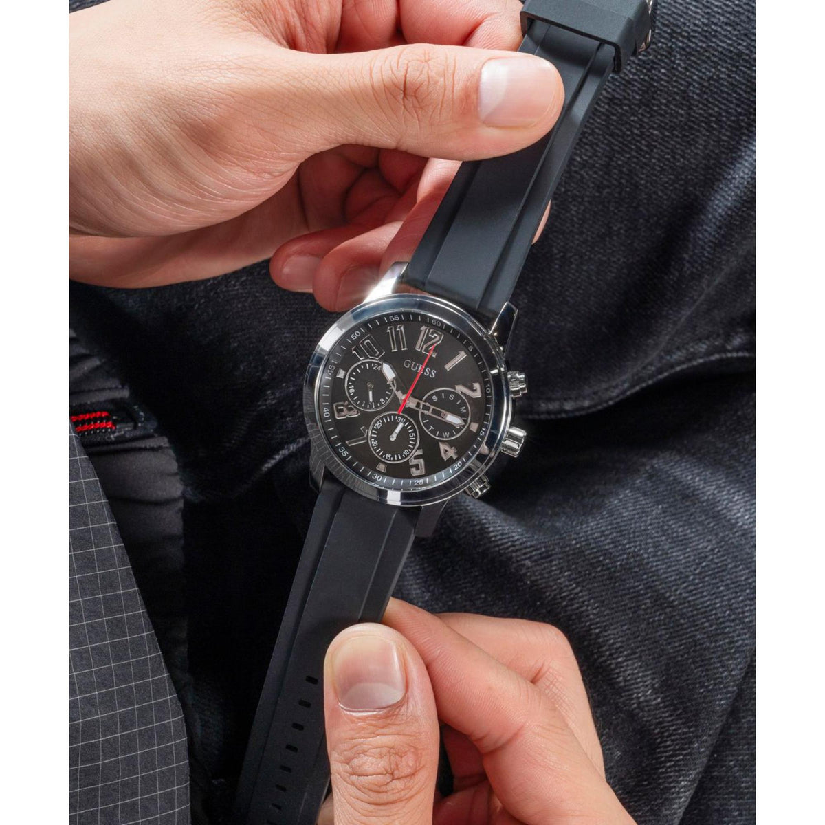 Men's black dial watch with black silicone strap, hand adjusting the clasp