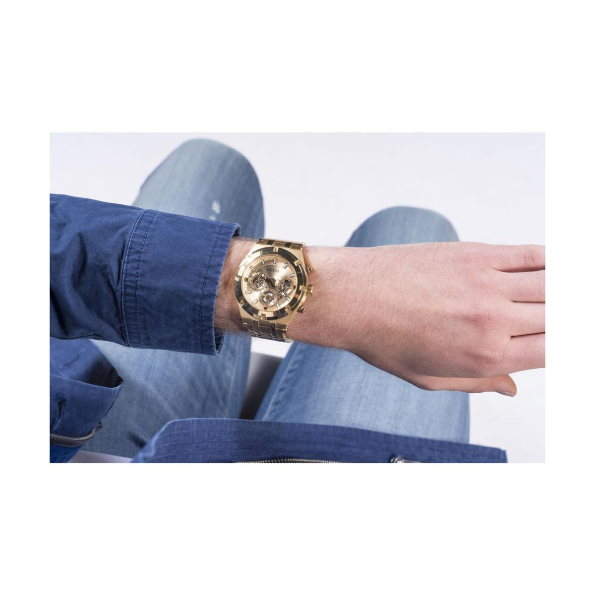 Gold-tone men’s skeleton watch worn with a blue long-sleeve shirt and steel bracelet.
