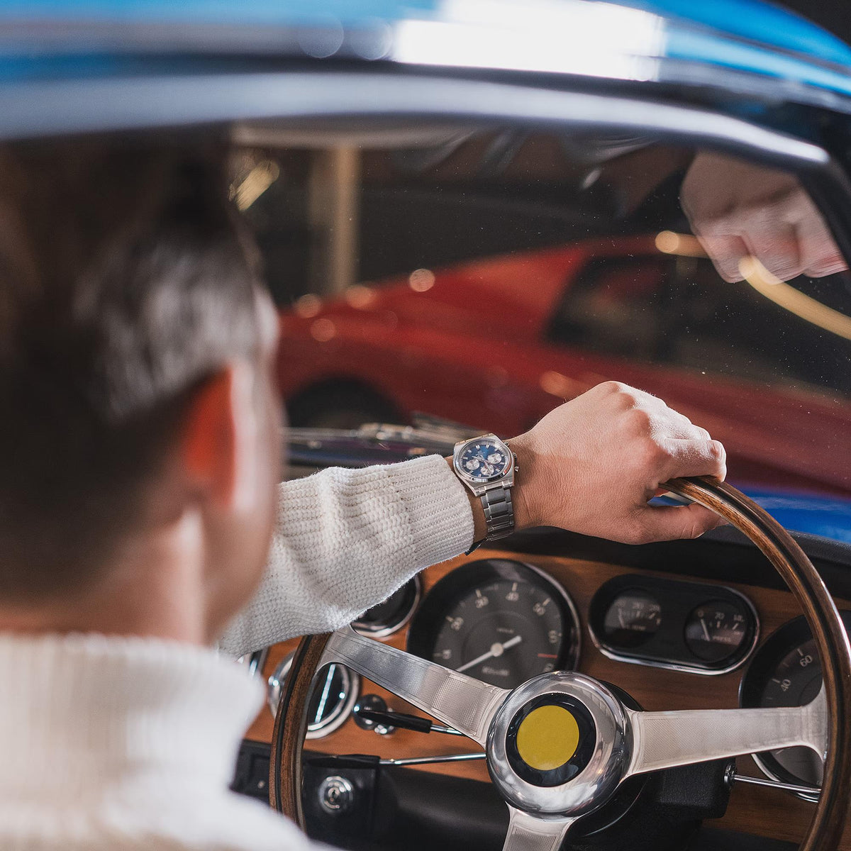 Men's chronograph watch with blue dial and steel bracelet, visible on driver’s wrist