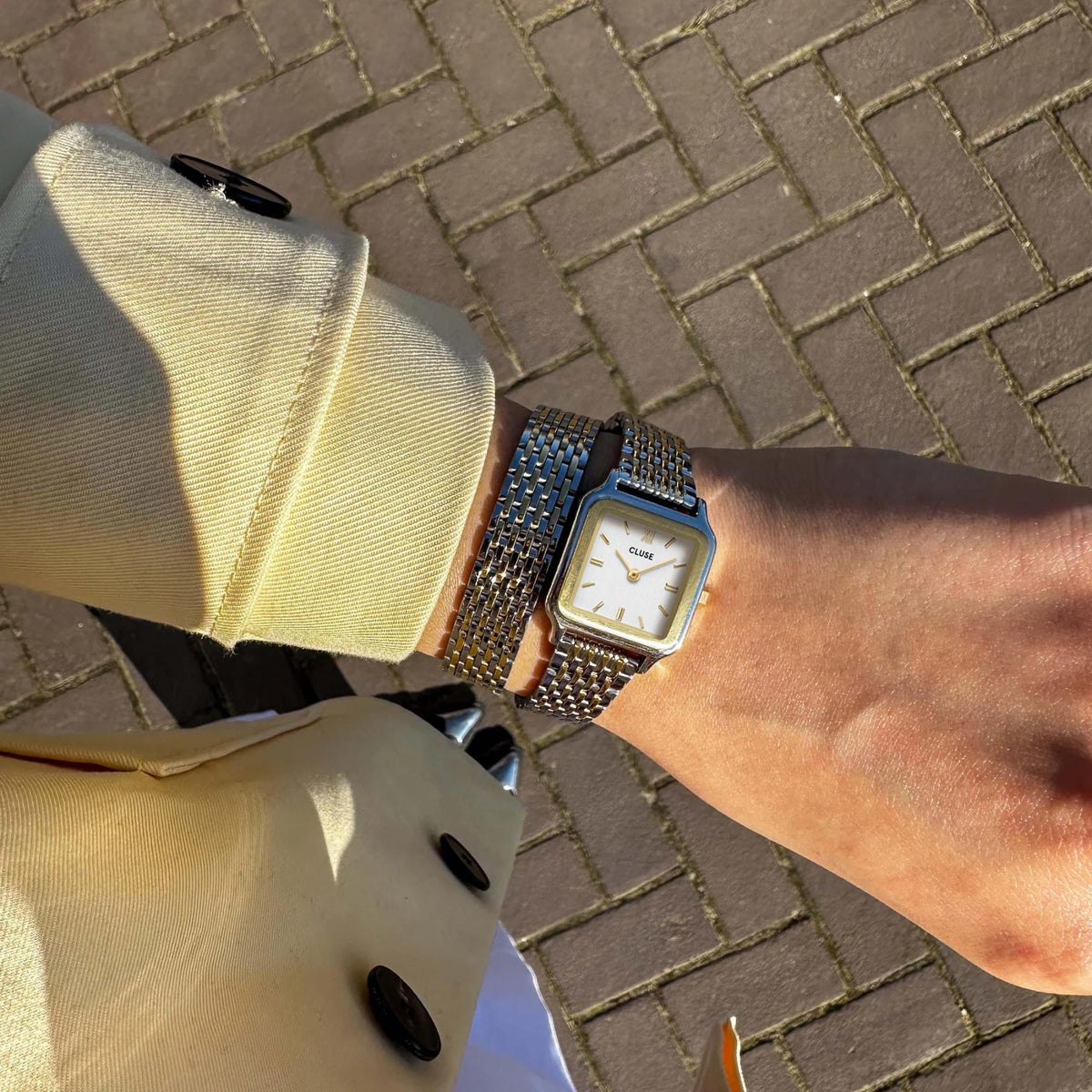 Two-tone mesh watch on wrist with square white dial and gold markers