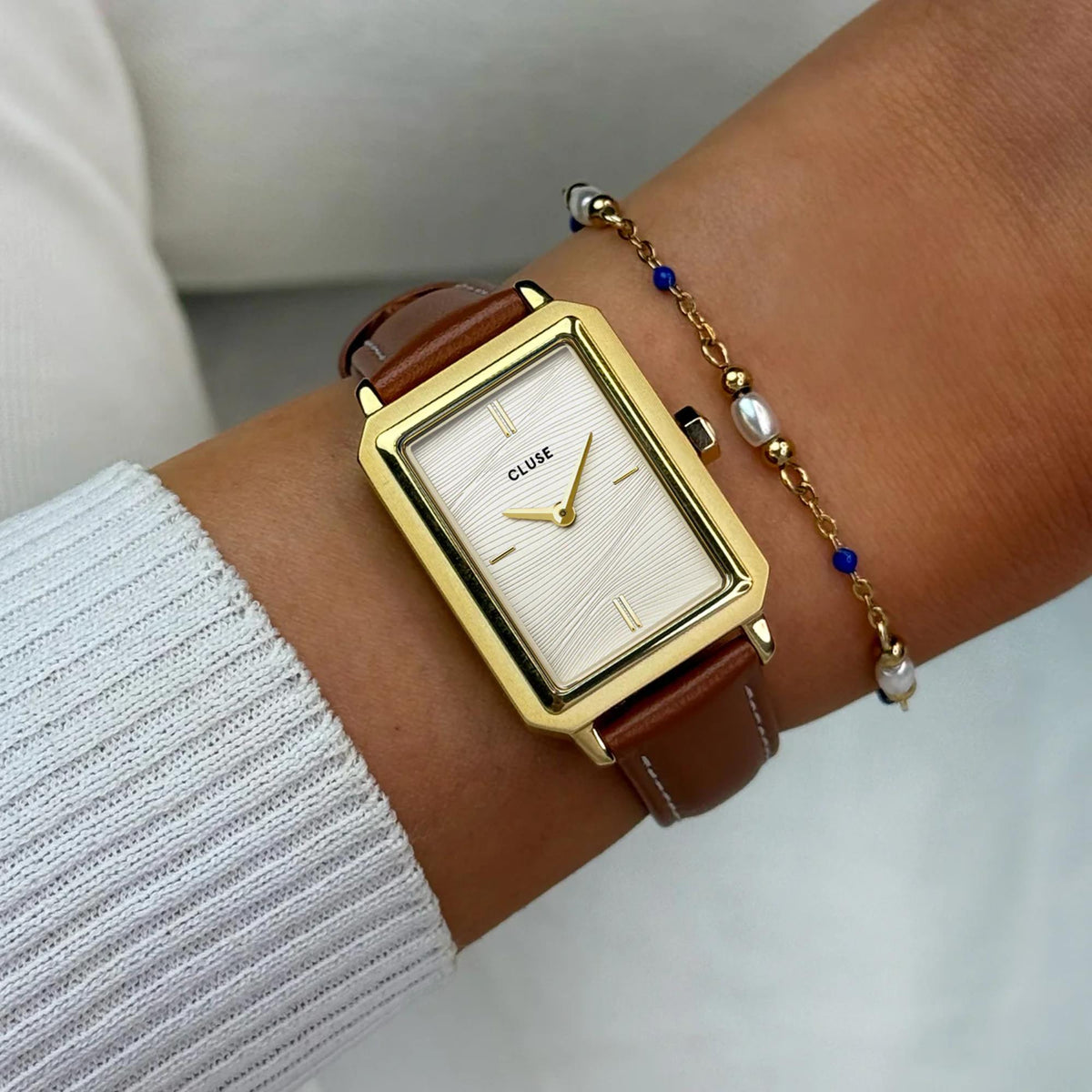 Close-up of women's gold square watch with white dial and brown leather strap