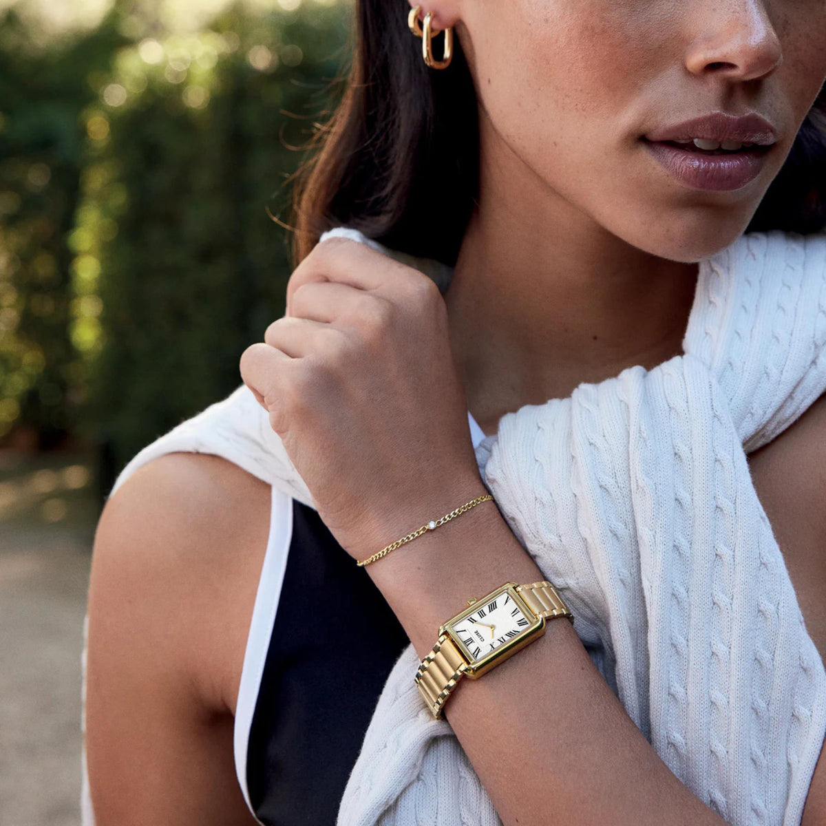 Gold-tone rectangular watch with white dial and roman numerals; metal link bracelet on arm