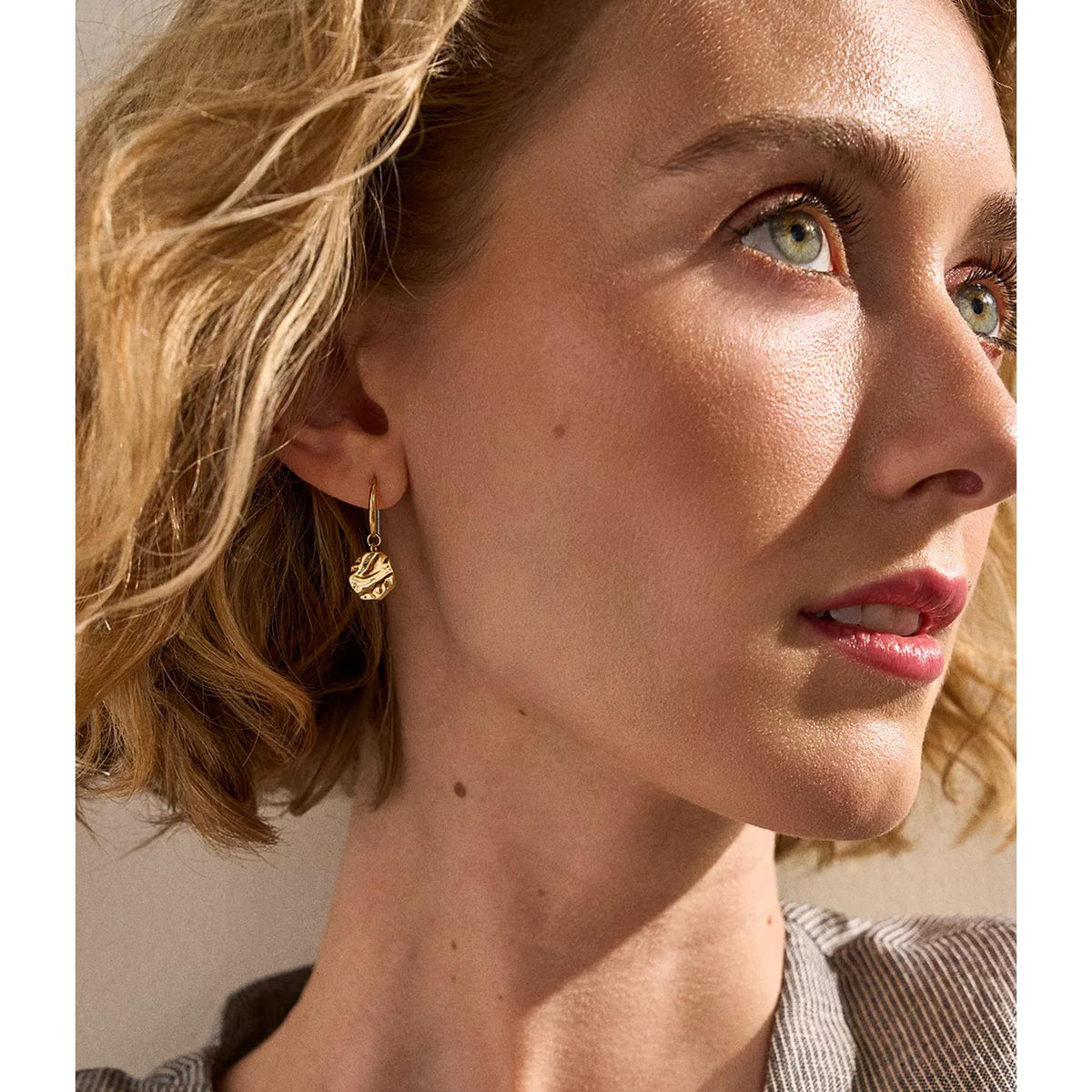 Gold-tone wave medallion drop earrings on model, dangling from small hooks