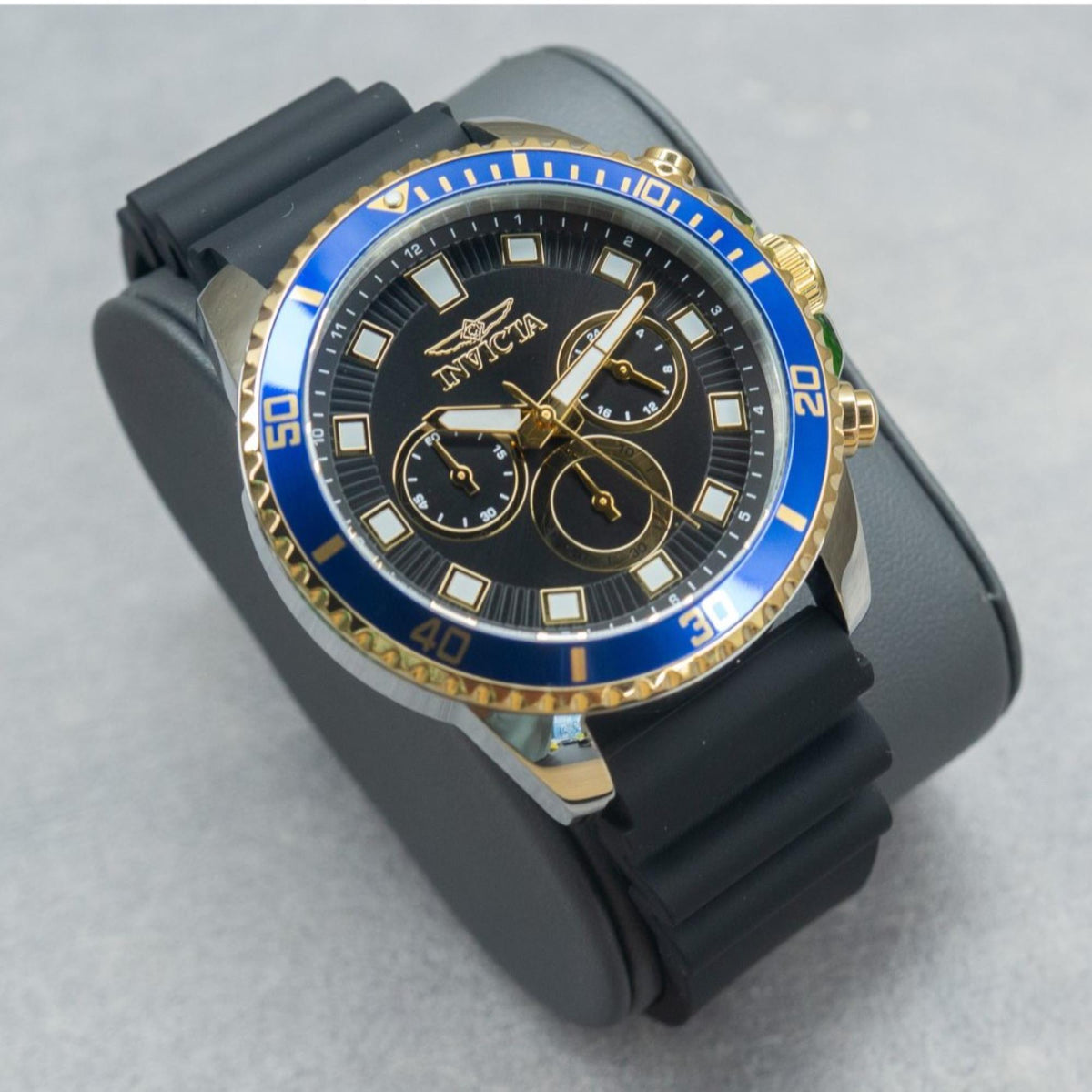 Angled men's Invicta chronograph watch with black dial, blue bezel, black silicone strap