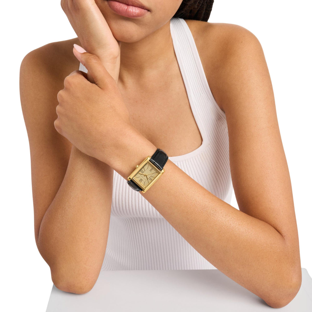 Michael Kors Essex MK4965 womens watch styled on a wrist, displaying the gold dial rectangular case and black leather strap