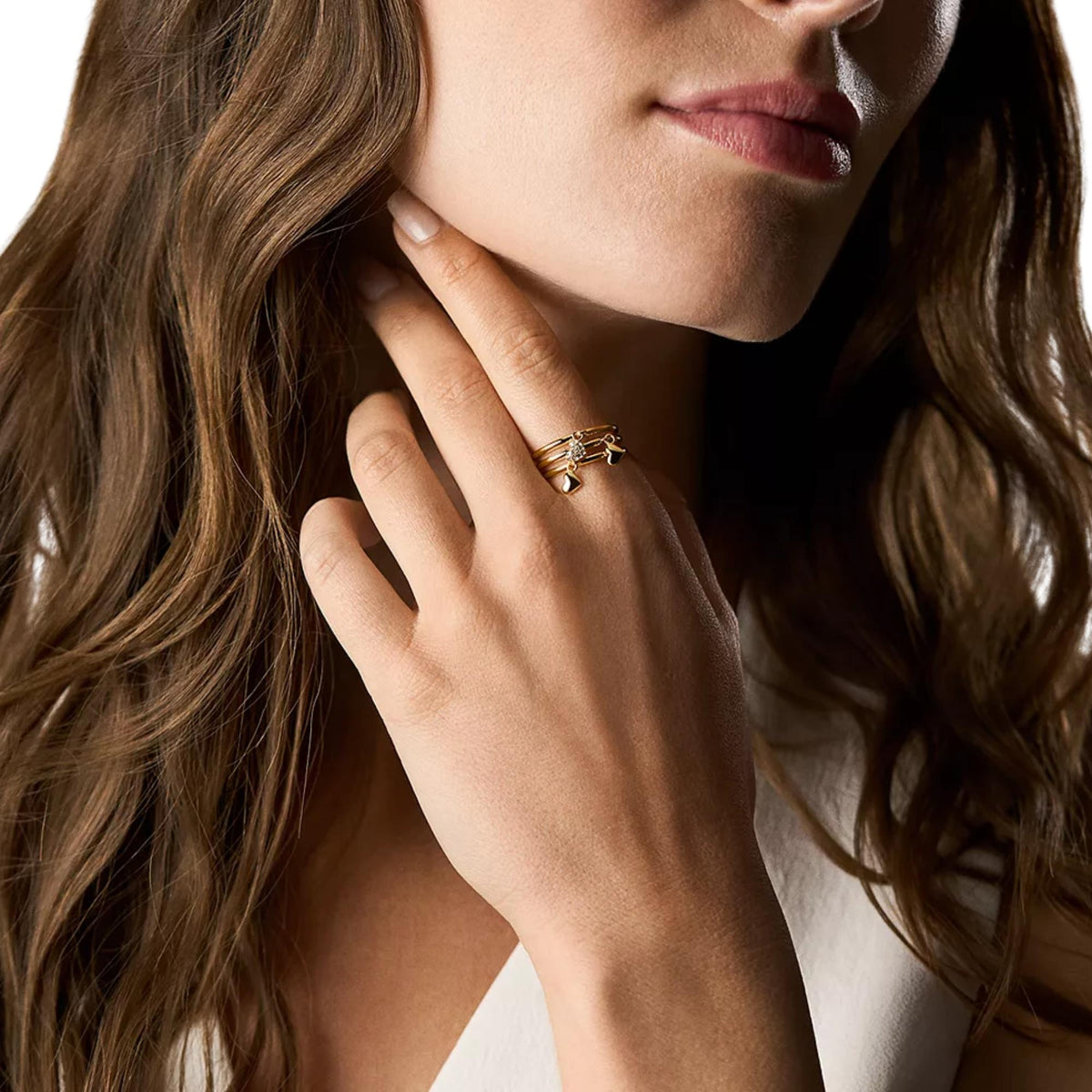 Gold-tone layered ring on finger with small heart charm and stone cluster