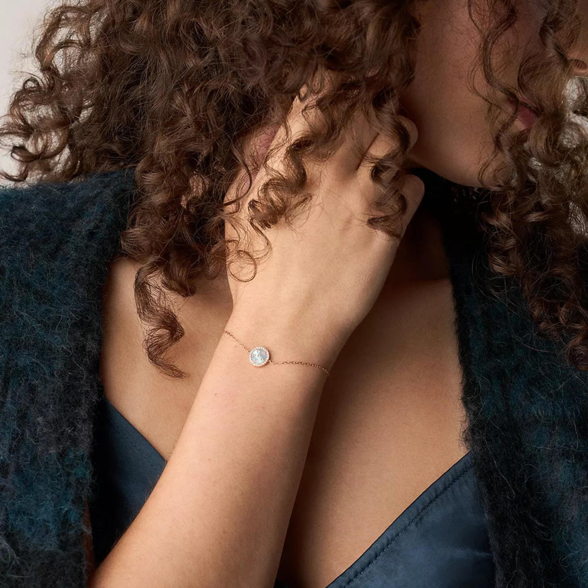 Rose gold-tone bracelet on wrist with small round blue mother-of-pearl charm and chain