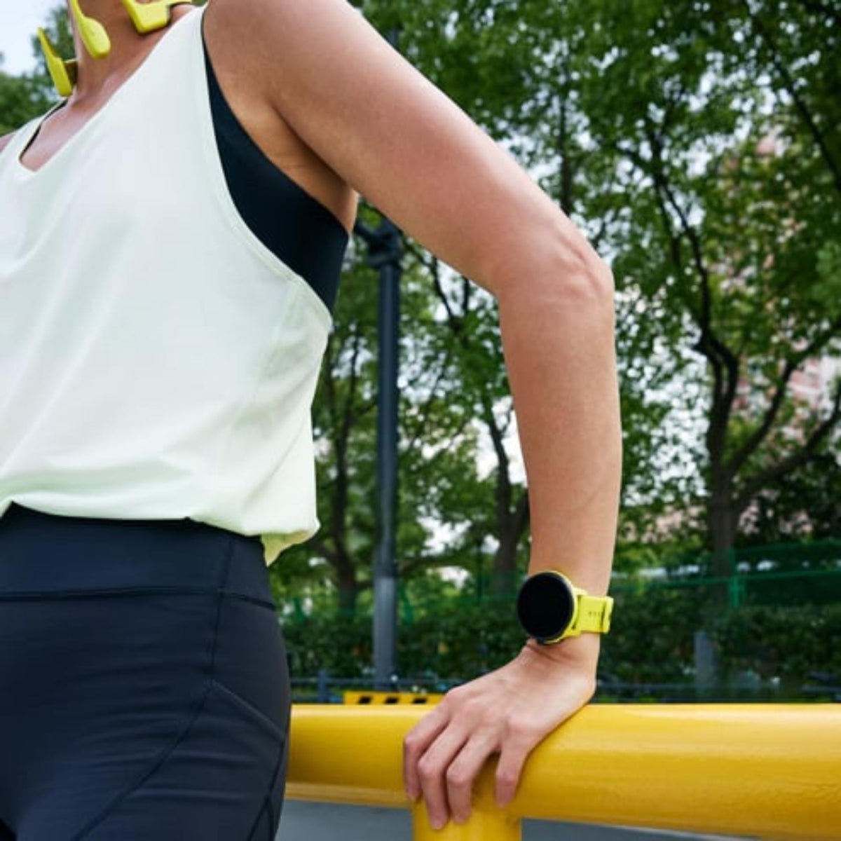 An athlete leaning against a railing while wearing the lime green smart fitness watch on their wrist