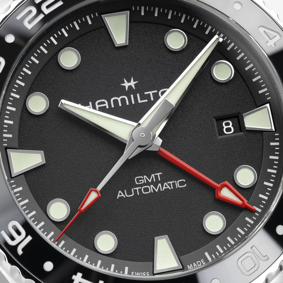 Close-up of black GMT automatic watch dial with luminous markers, hands, and date window