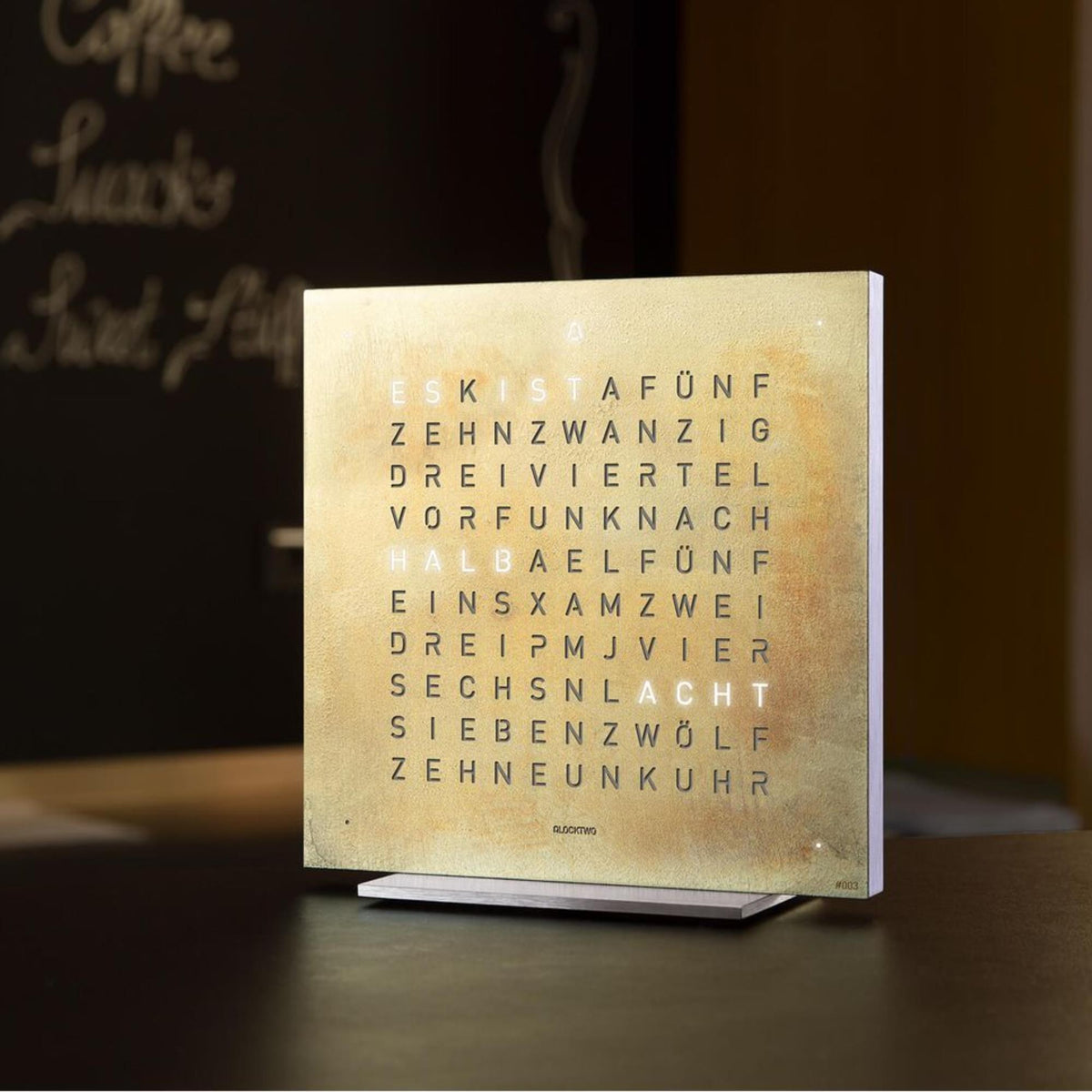QLOCKTWO Earth English table clock on table, front panel shows glowing hour words