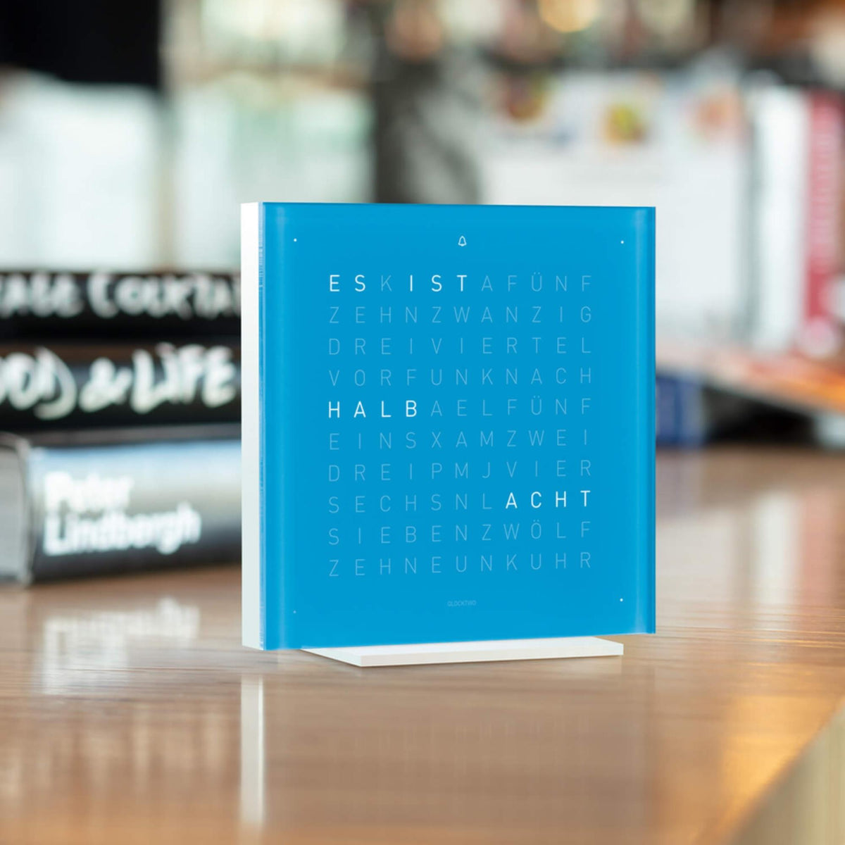 Blue QLOCKTWO table clock with word grid letters and white base on tabletop
