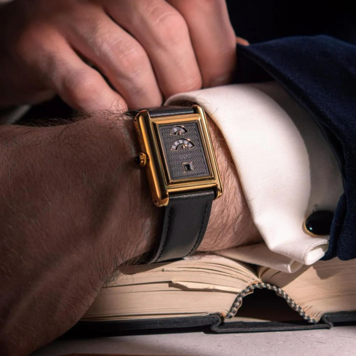 Automatic wristwatch on wrist; gold rectangular case with black dial and black leather strap