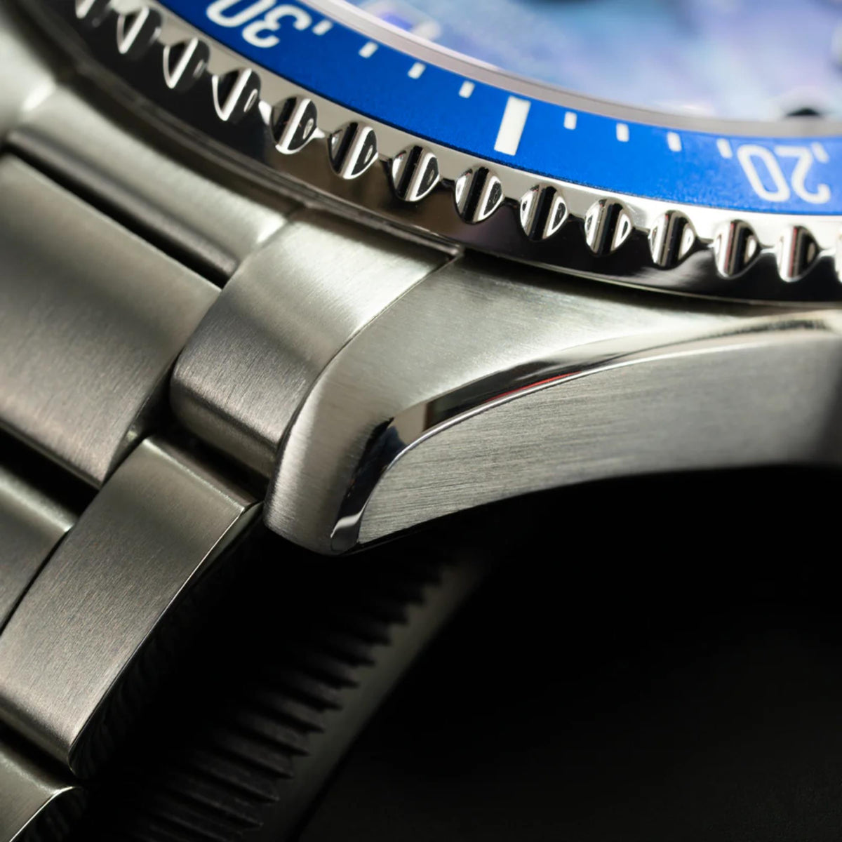 Steel watch case close-up with crown and blue bezel edge detail