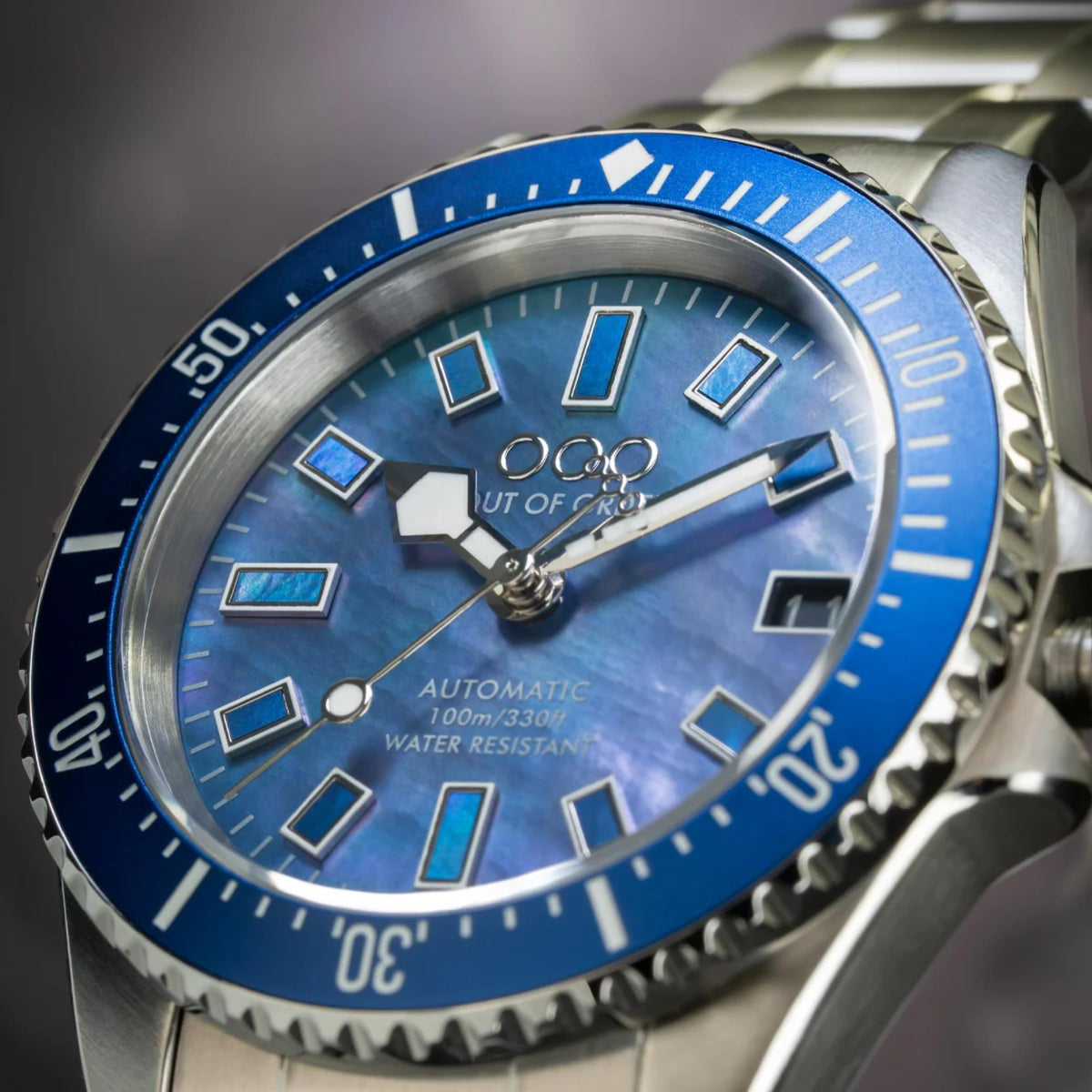 Men's automatic watch dial close-up with blue sunburst texture and rectangular hour markers