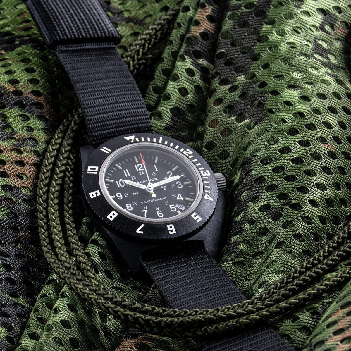 Marathon Navigator WW194013BK-0001 quartz watch resting on camouflage patterned fabric background