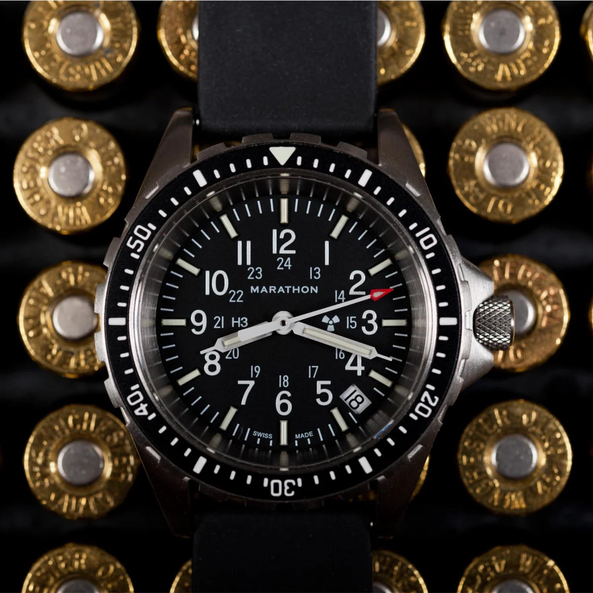 Marathon MSAR WW194027SS-0130 mens quartz watch macro shot showing black dial with date aperture and rubber strap on metallic background