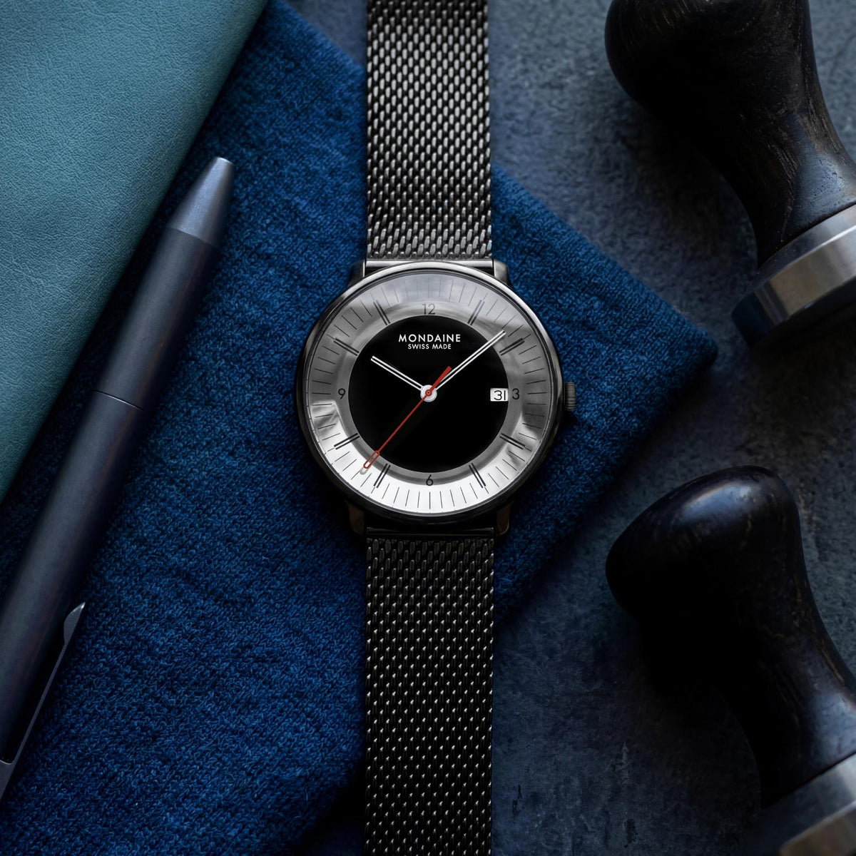 Mondaine Doppio Mirror MLE.41280.SM flat lay view featuring black dial mens quartz watch with mesh strap alongside accessories