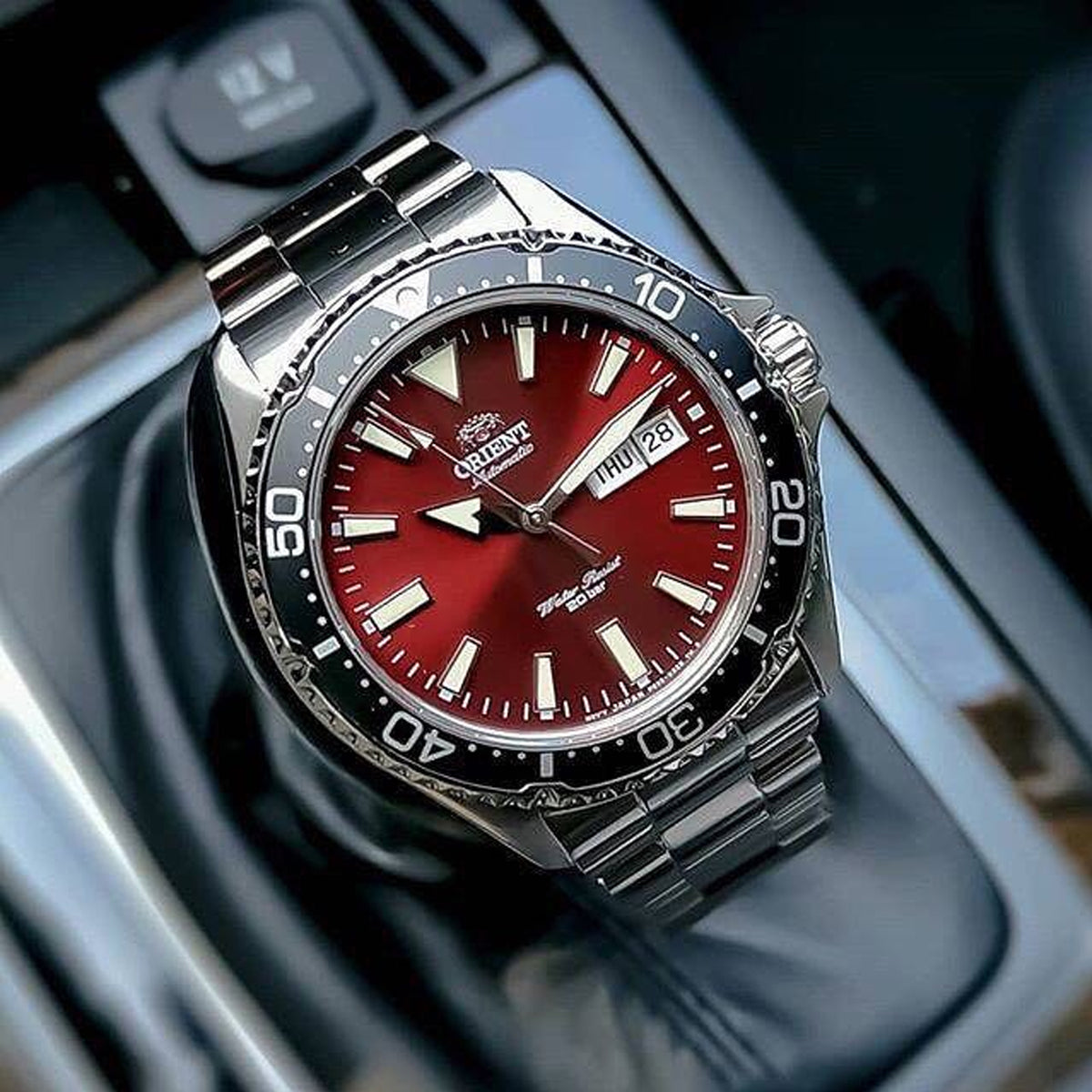 Orient automatic sports diver watch featuring a bold red sunburst dial, black rotating bezel, and stainless steel bracelet