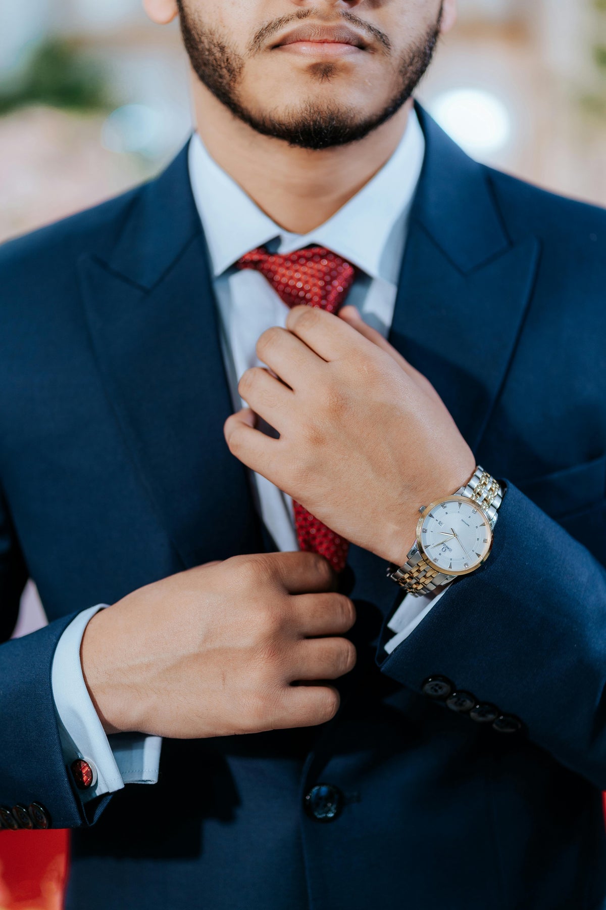 Man adjusting his red tie with a gold watch, wearing a blue suit.