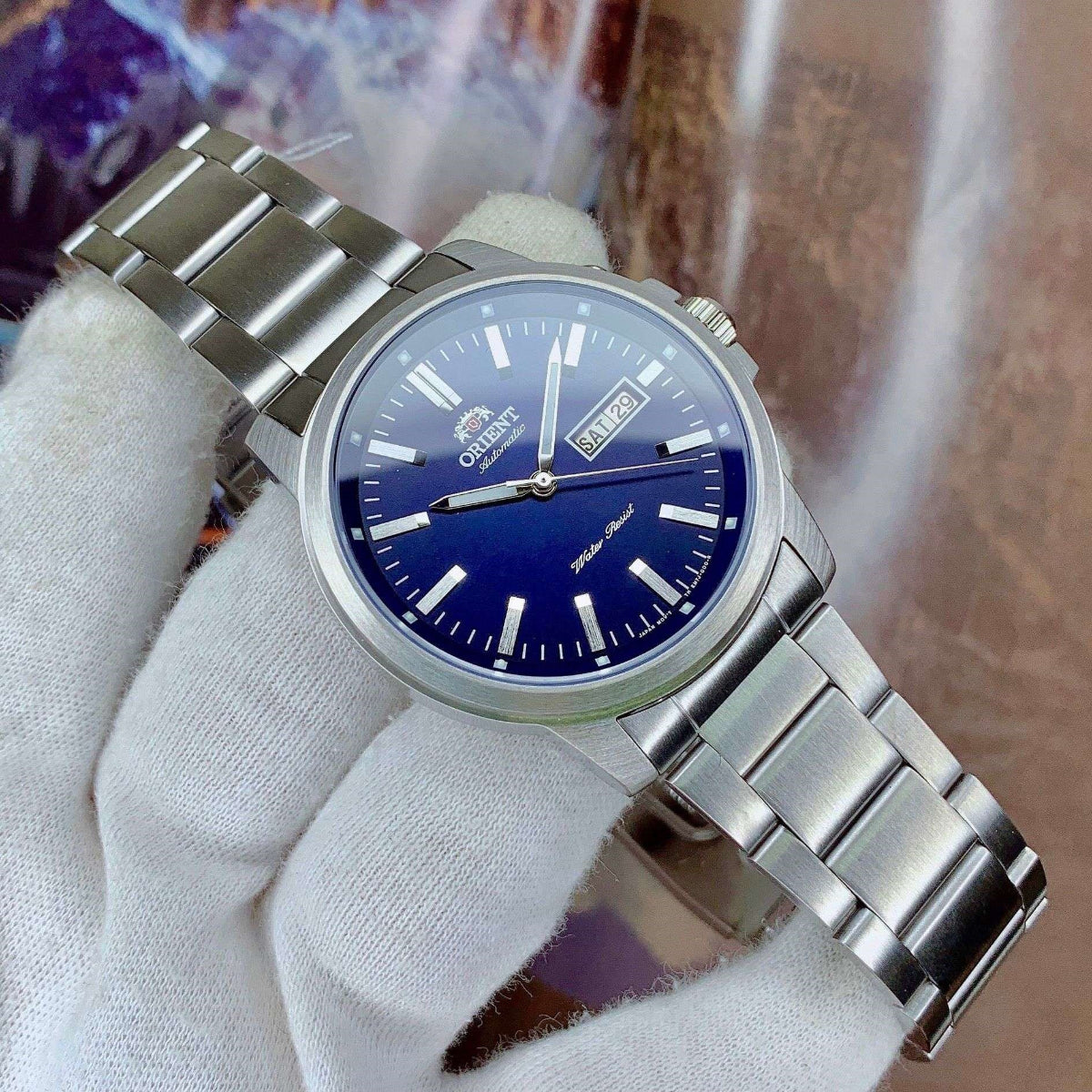 Orient Contemporary RA-AA0C02L39B wristwatch with blue dial held by a gloved hand against a blurred background