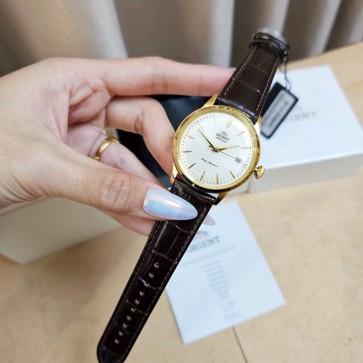 Hand holding Orient Bambino Version 7 Classic RA-AC0M01S30B wristwatch with a brown leather strap and gold-tone stainless steel case