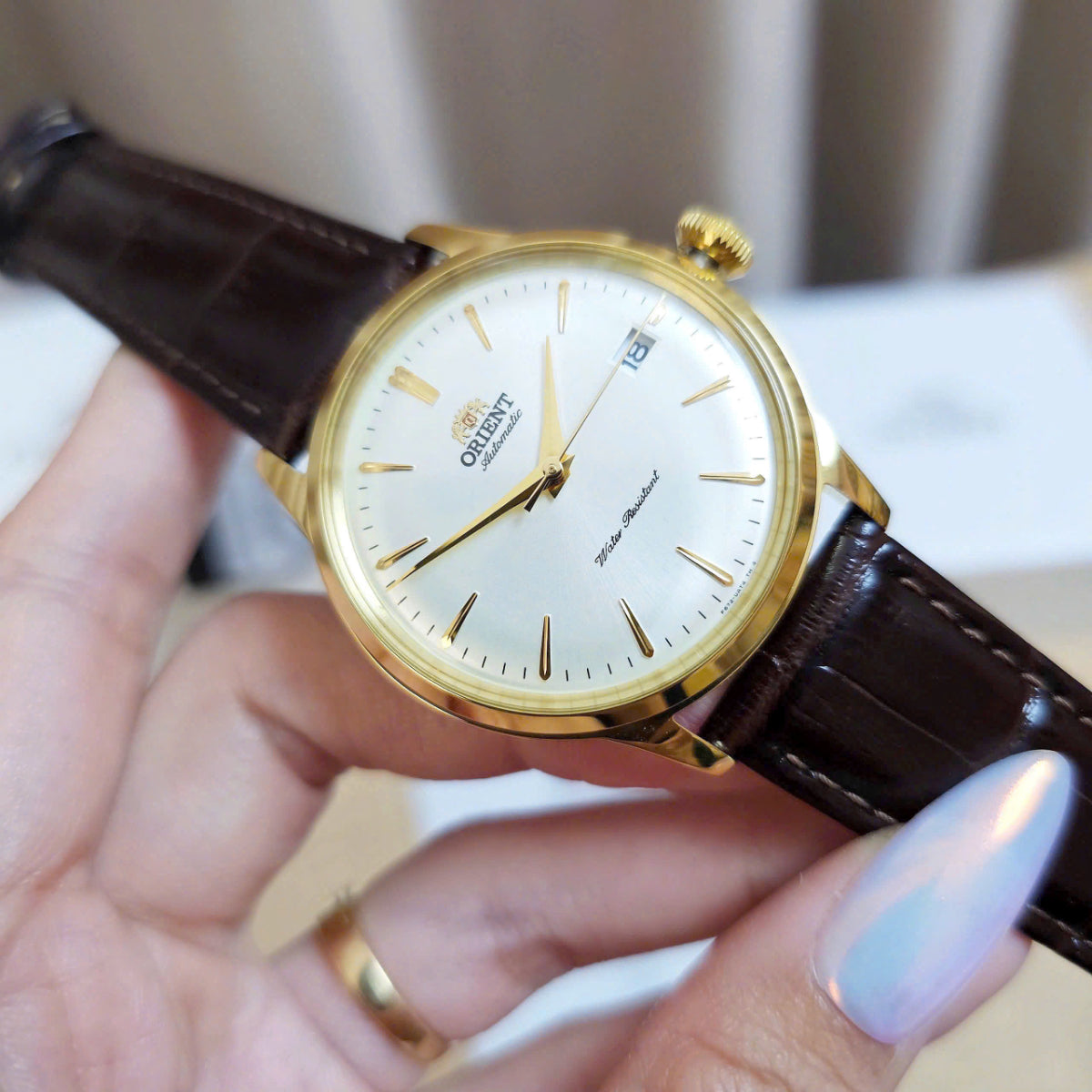 Orient Bambino Version 7 Classic RA-AC0M01S30B wristwatch with brown leather strap held by a hand