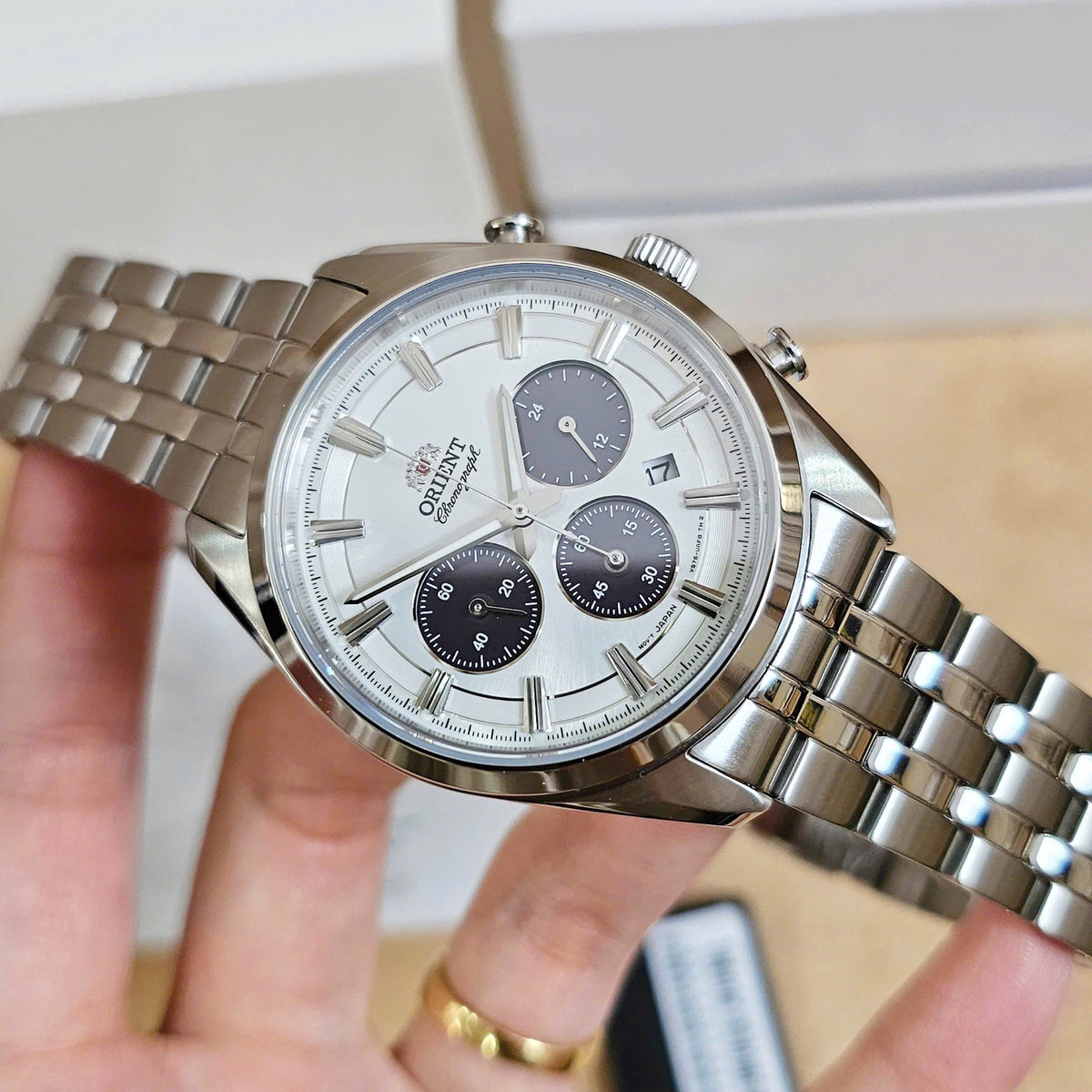Men’s solar chronograph watch on wrist with white dial, steel bracelet, and subdials