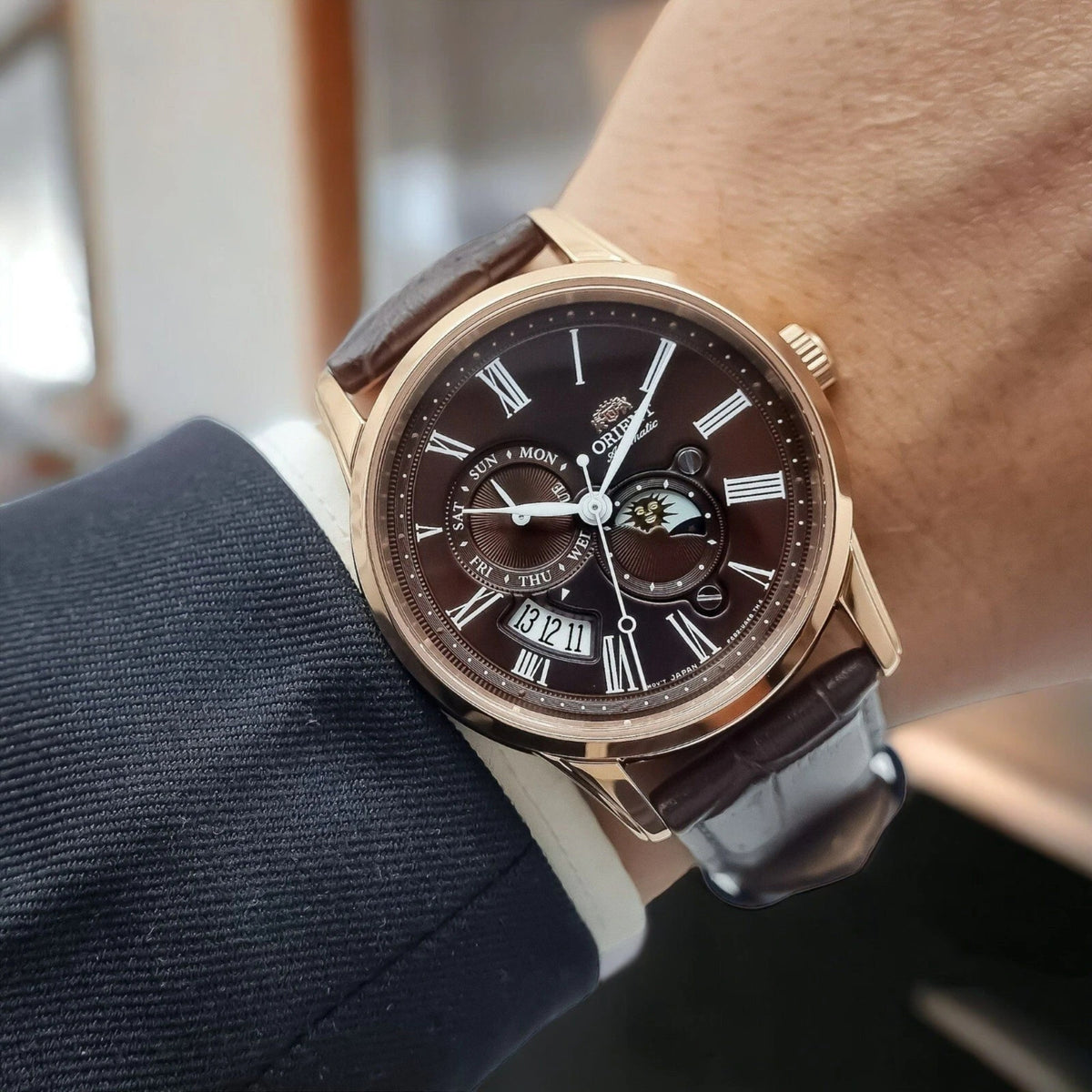 Orient Bambino RA-AK0009T30B automatic wristwatch on wrist, brown leather strap and rose-gold case with dark dial details
