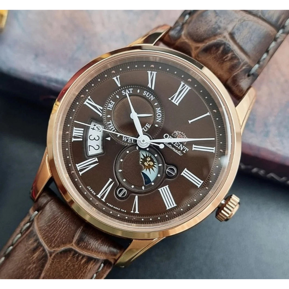 Orient Bambino Sun and Moon RA-AK0009T30B automatic watch close-up with brown dial, sub-dials, and brown leather strap