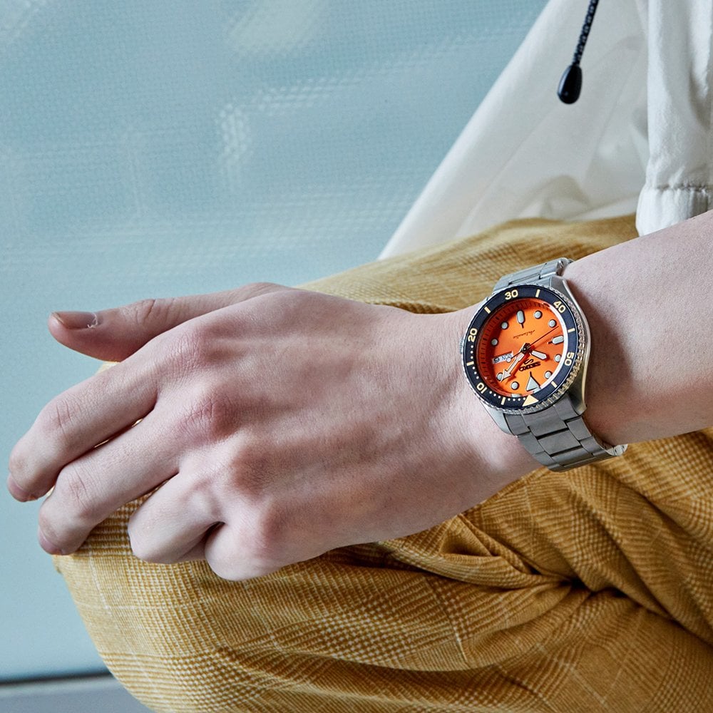 Men's Seiko watch on wrist with orange dial, black bezel, stainless bracelet
