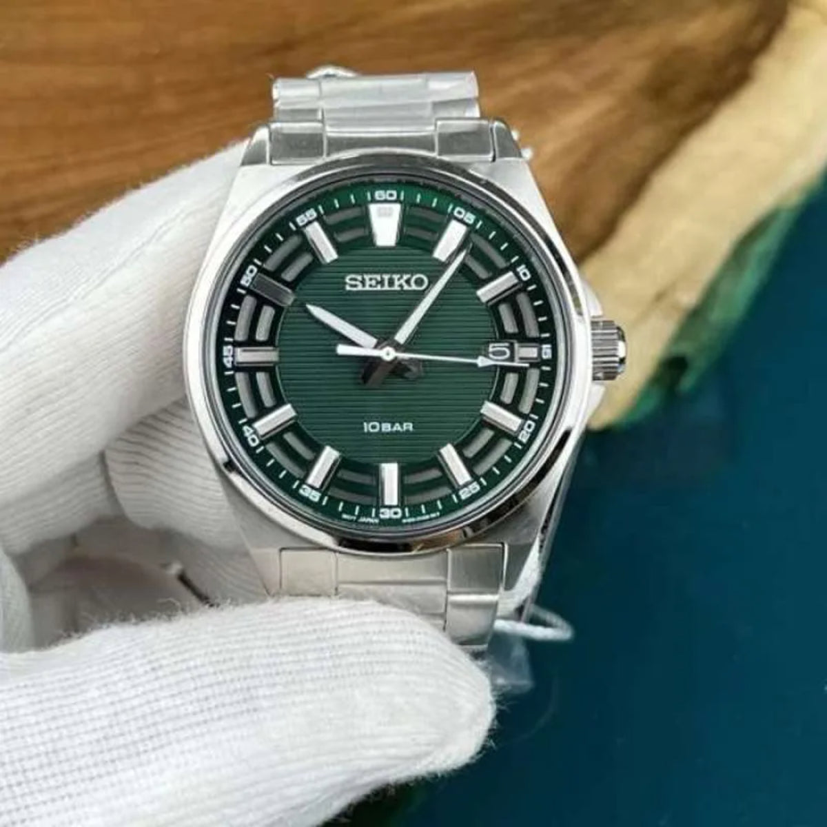 Gloved hand holding the Seiko Essentials SUR503P1 wrist watch to highlight its emerald green face and silver indices