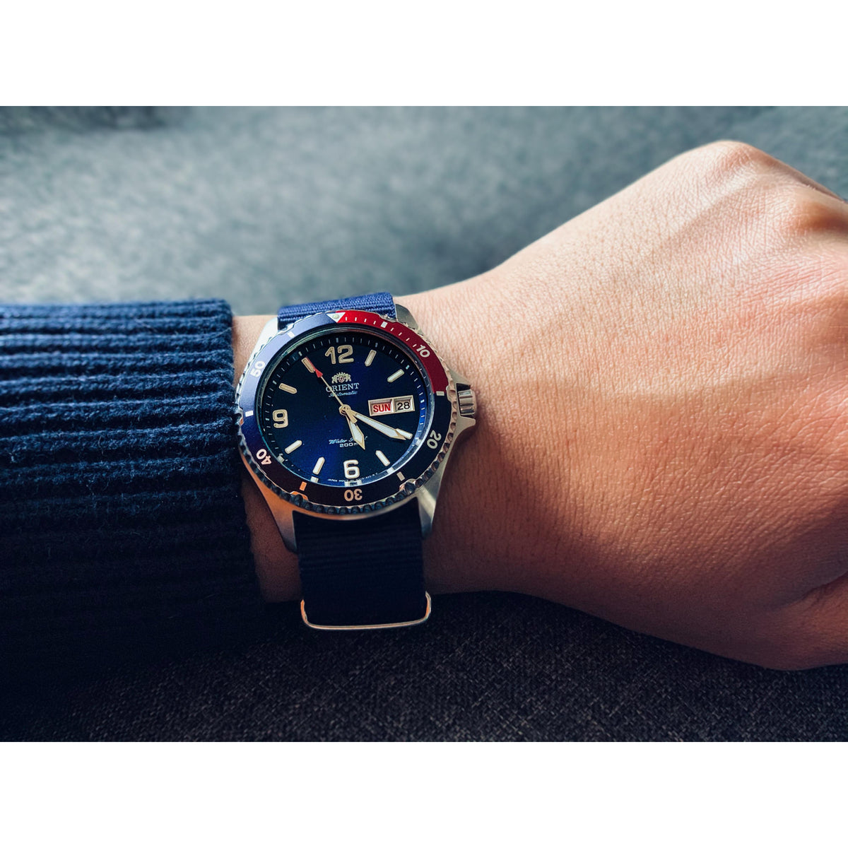 Men's stainless automatic diver watch with blue dial, red-and-blue bezel, on wrist