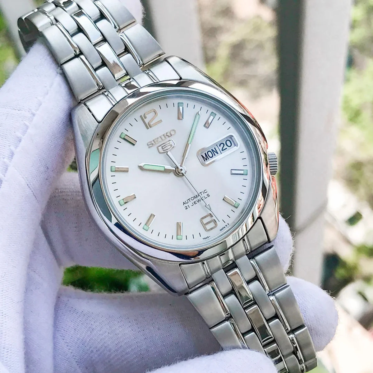 Seiko 5 stainless steel watch SNK385K1 on hand with a silver dial, metal bracelet, and day-date window