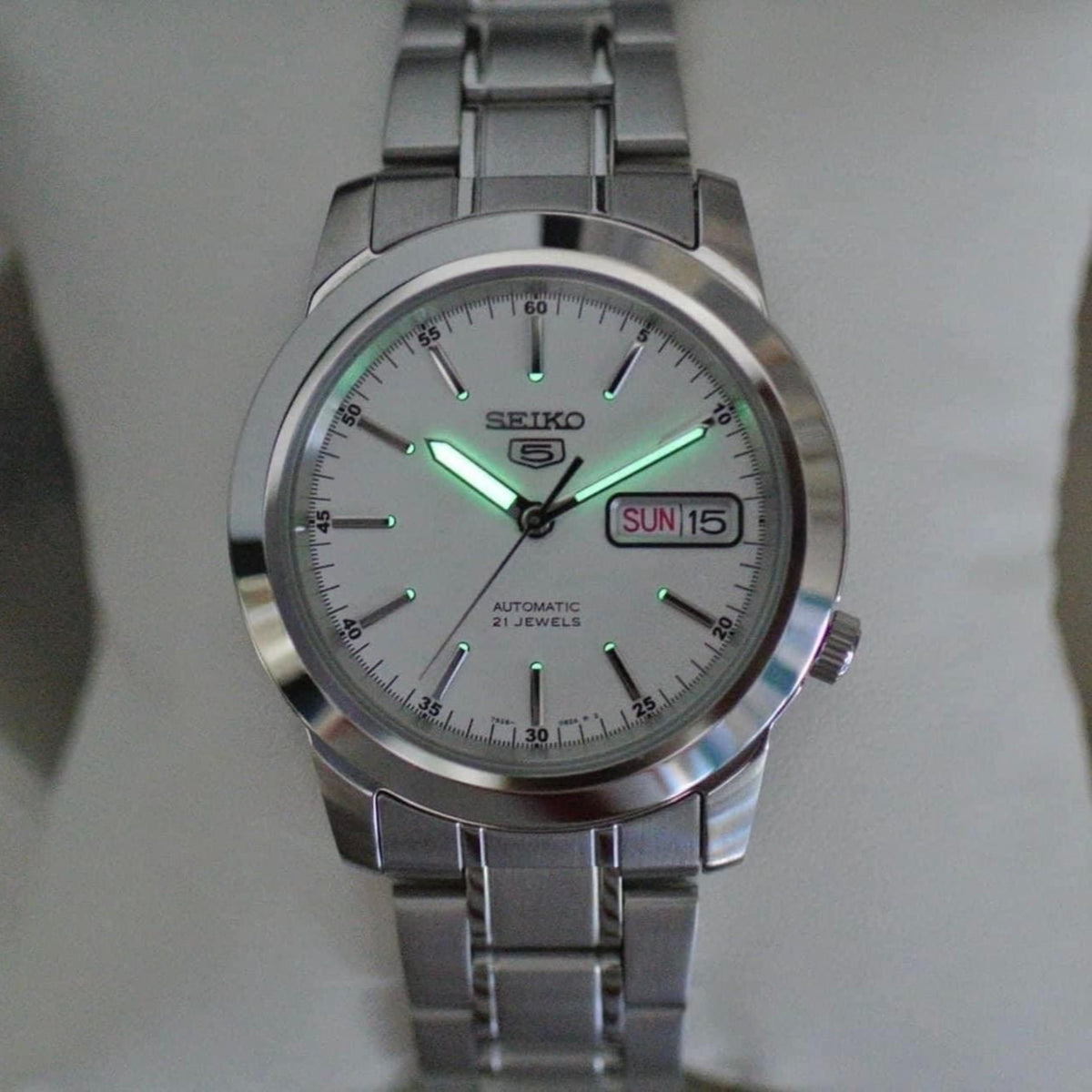 Seiko 5 Automatic SNKE49K1 front perspective showing luminous watch hands glowing on white dial