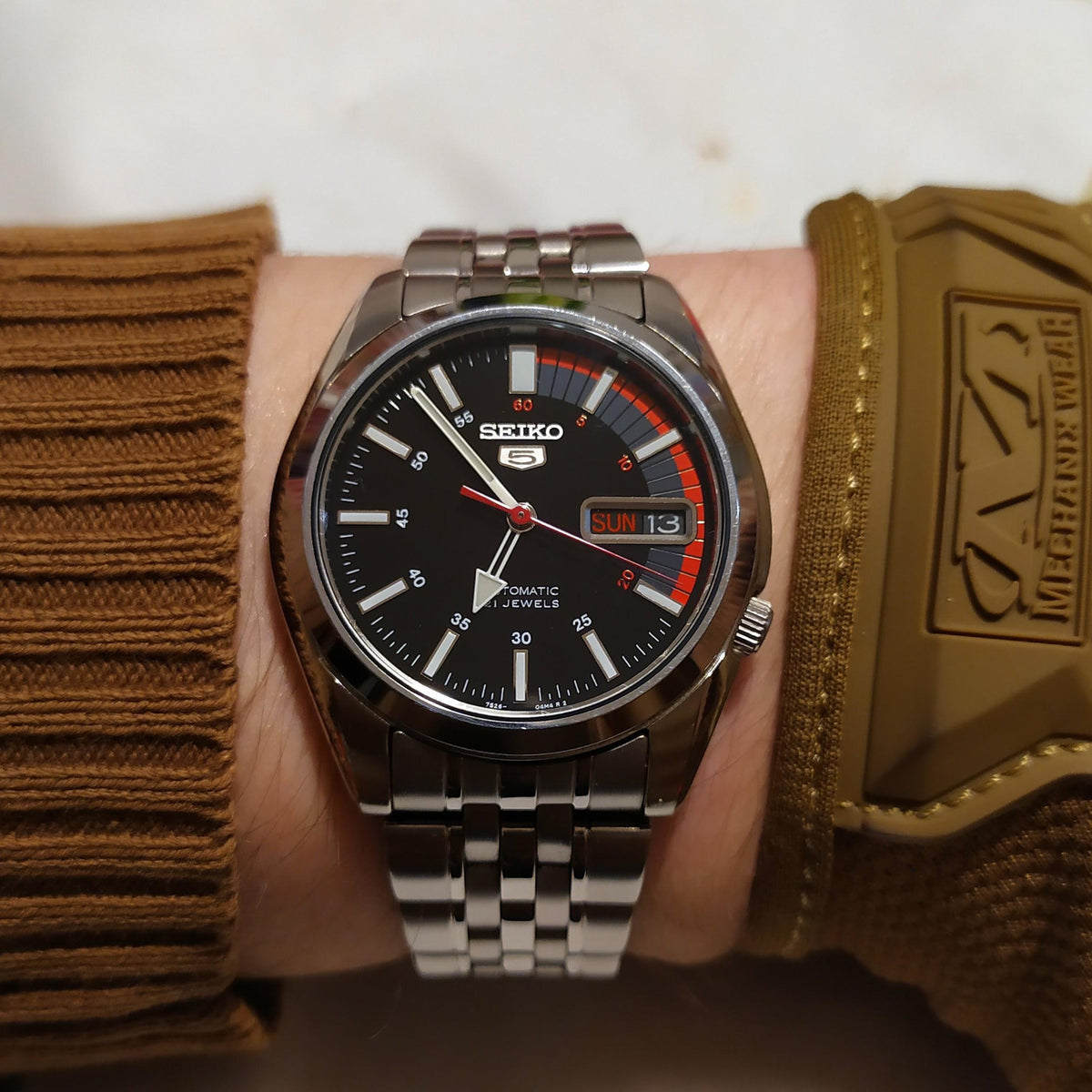 Seiko 5 SNK375K1 watch with black dial, red accents, and day/date display on steel bracelet