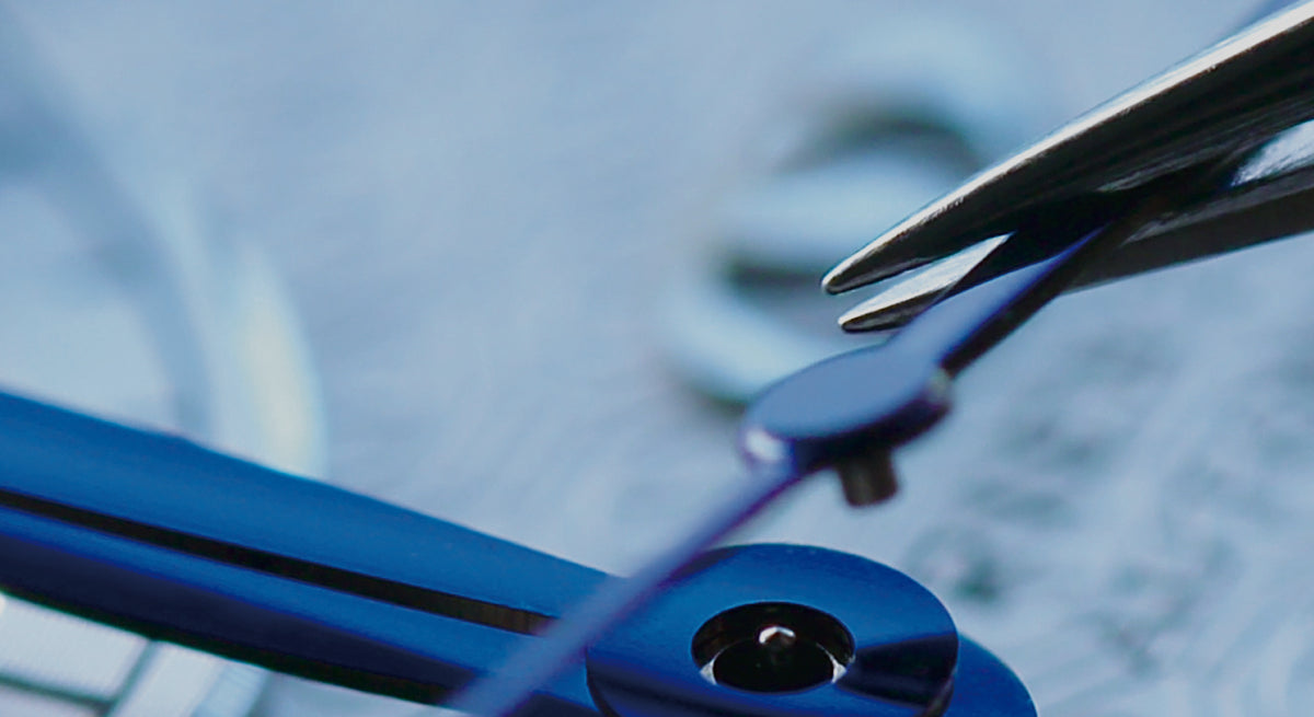 Macro view of watchmaker tweezers precisely aligning thermal blued watch hands on an Orient Star automatic watch movement