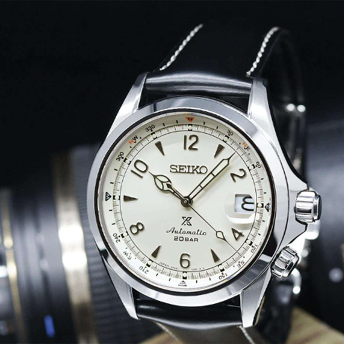Close-up of men's automatic watch face: cream dial, silver bezel, black leather strap