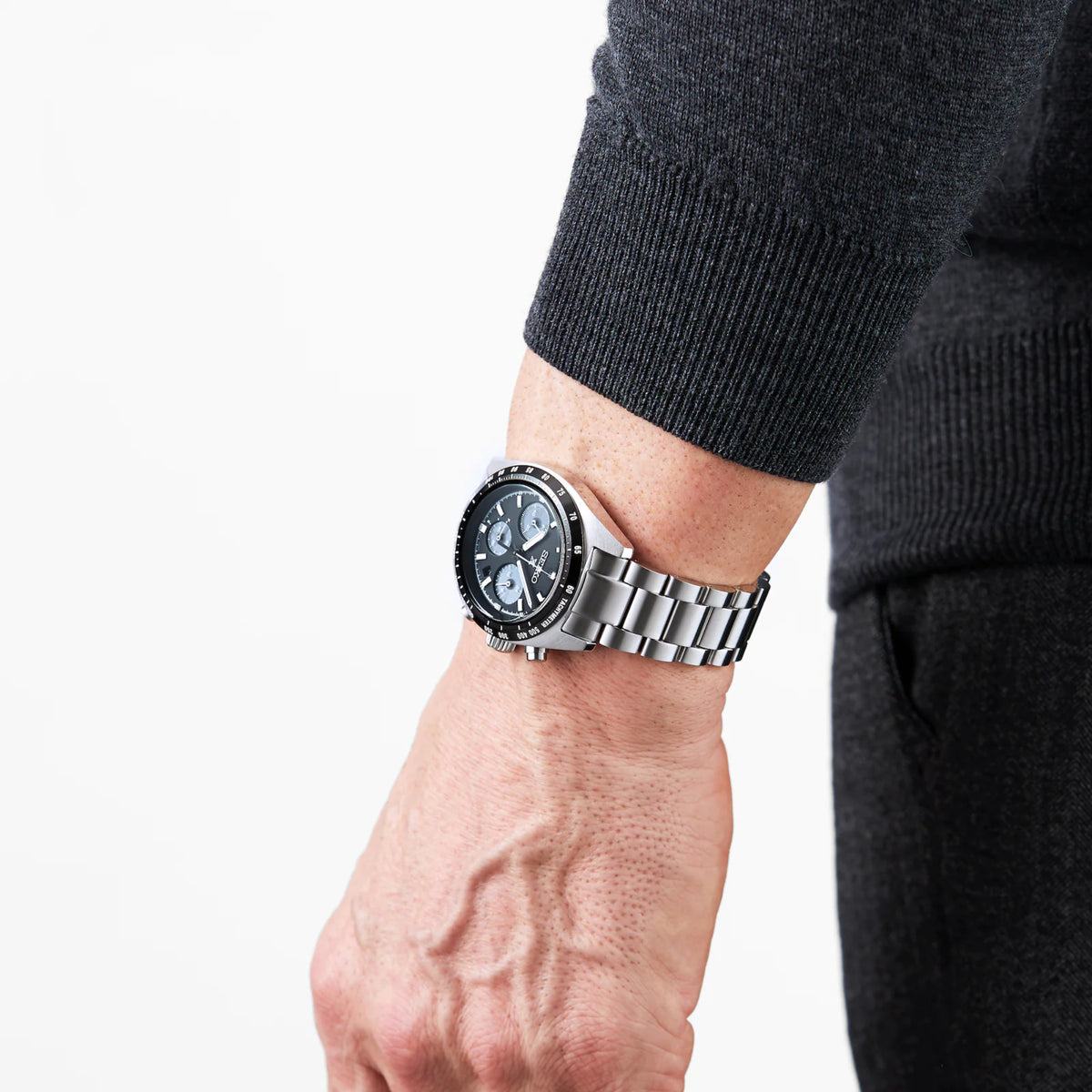 Men's chronograph watch on wrist showing black dial and polished stainless bracelet