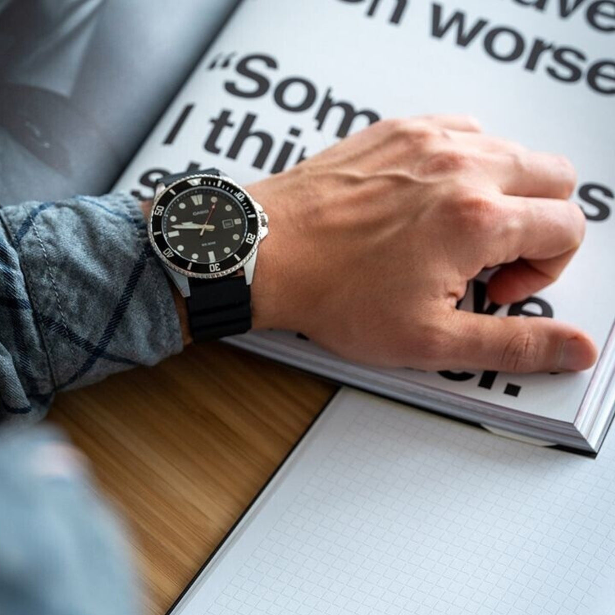Casio Timeless MDV-107-1A1VEF on a person's wrist over an open book, showcasing the rugged black resin strap and steel case