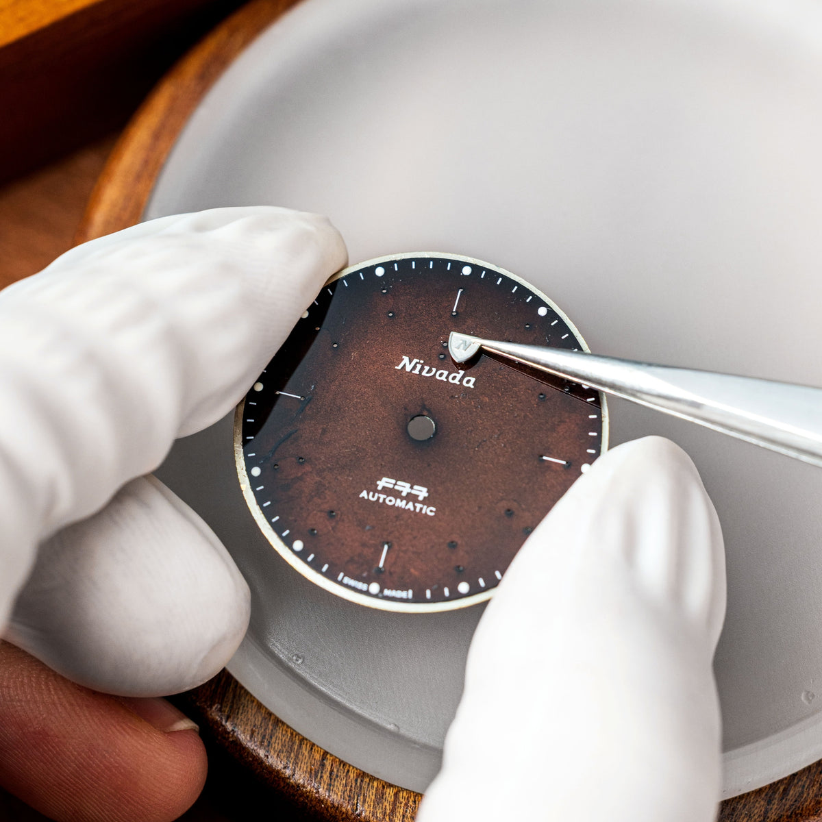 Nivada Grenchen F77 MK2 68060A77 craftsman placing brand logo on smoky quartz dial using tweezers