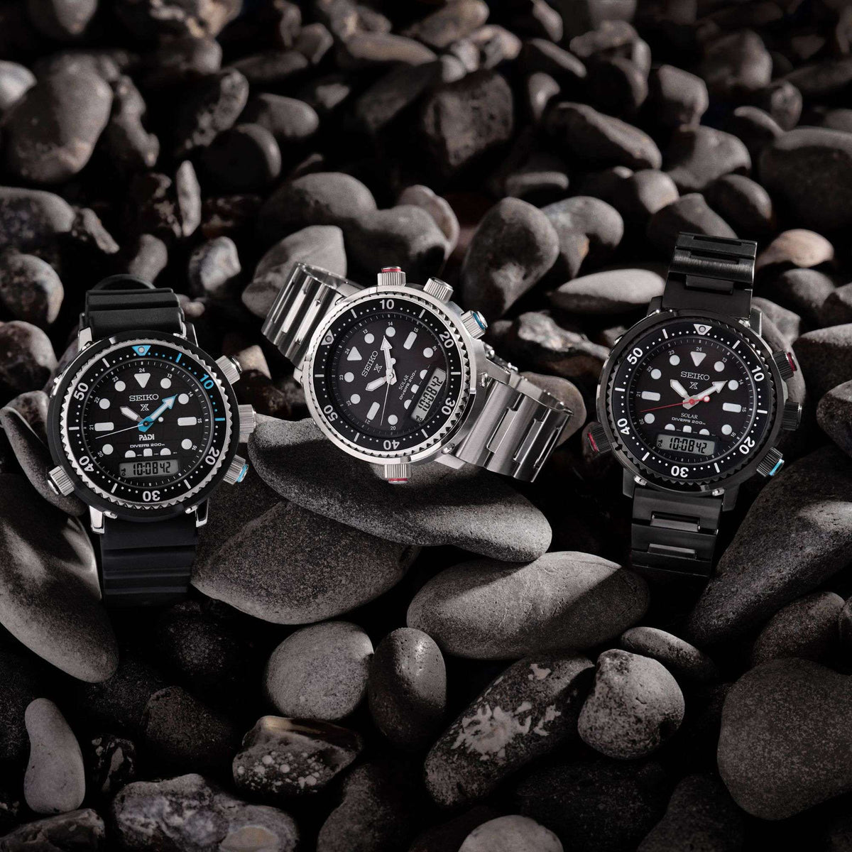 Three Seiko Prospex Solar watches on pebbles with a dark background