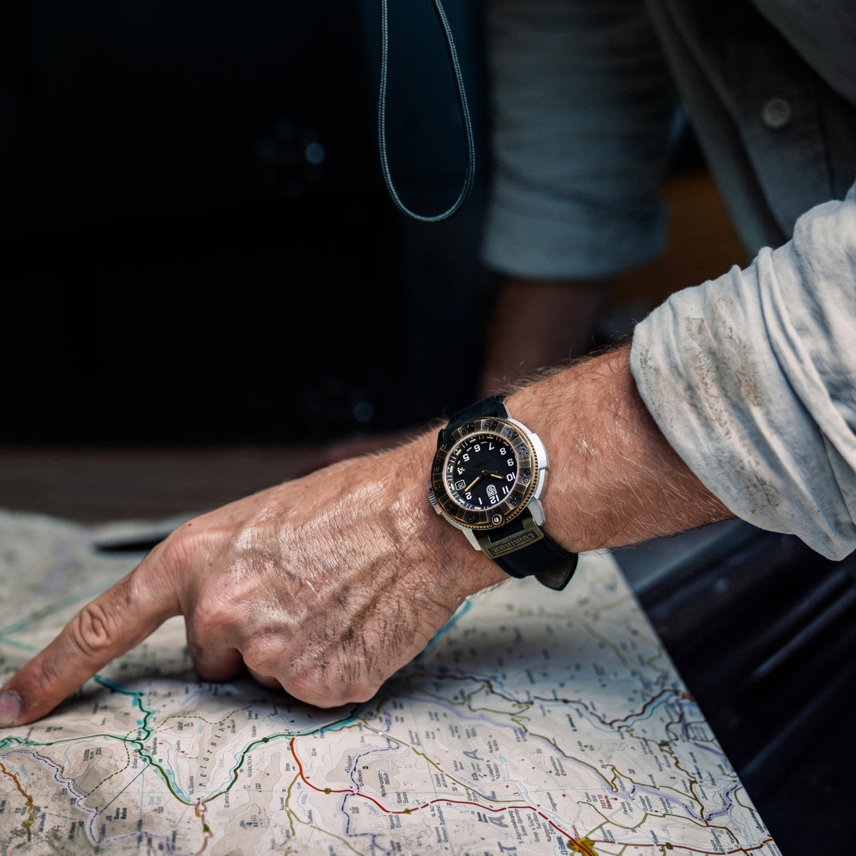 Close-up of a dirty hand pointing at a map, wearing a Luminox Adventure Watch XL.1301 watch with an antique bronze bezel and black strap