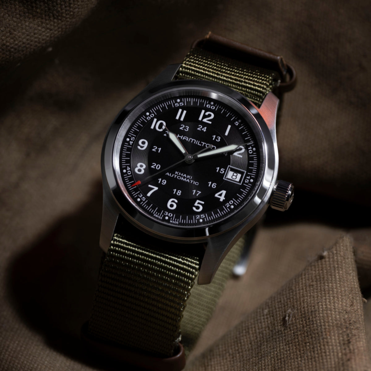 Round wristwatch with black dial, silver bezel, and olive-green NATO fabric strap